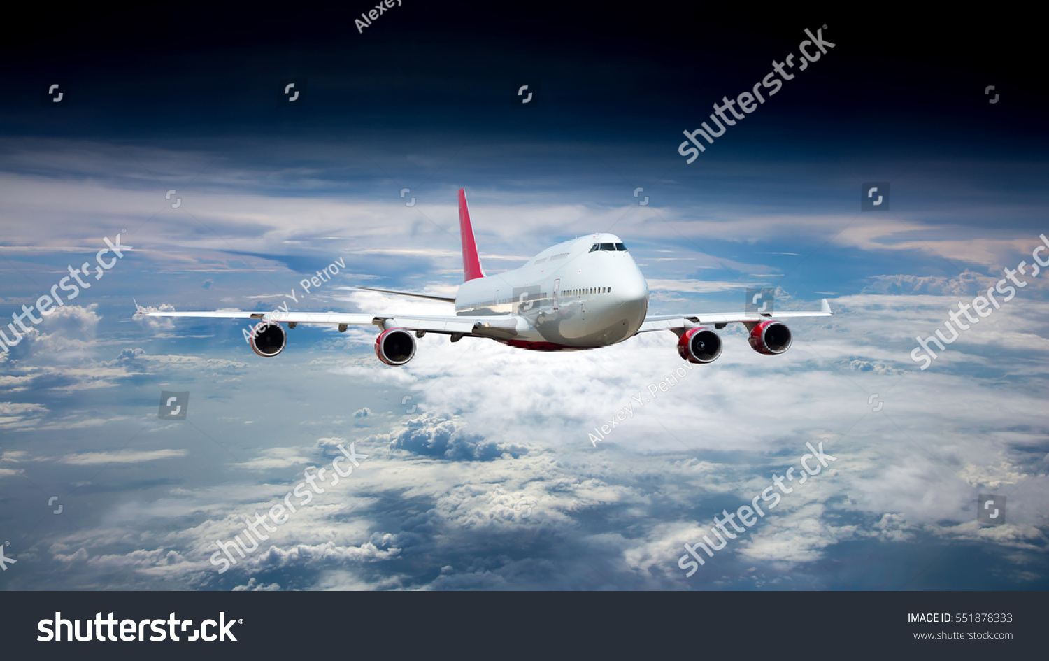 White passenger jet plane in the blue sky.  Aircraft flying high through the clouds. Airplane front view. #551878333