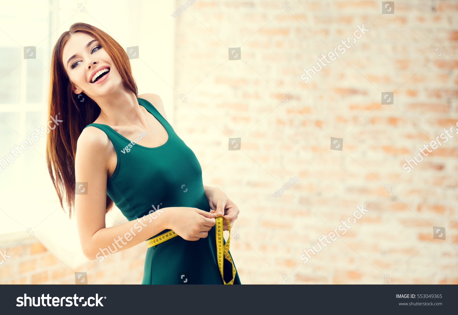 Young happy woman measuring her waist with a tape measure, at home, indoors. Caucasian model in healthy lifestyle, diet and  beauty concept shoot. Blank copyspace area for slogan or text message. #553049365