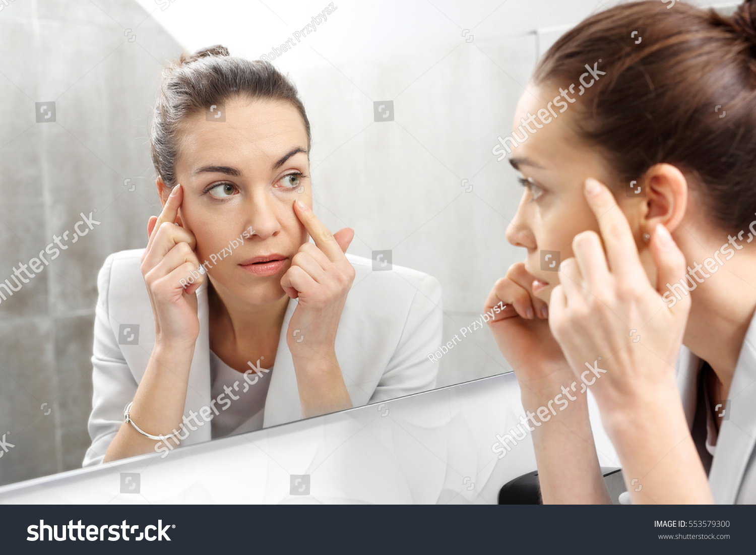 Reflection in the mirror.
Woman looks in the mirror noticing the first wrinkles
 #553579300