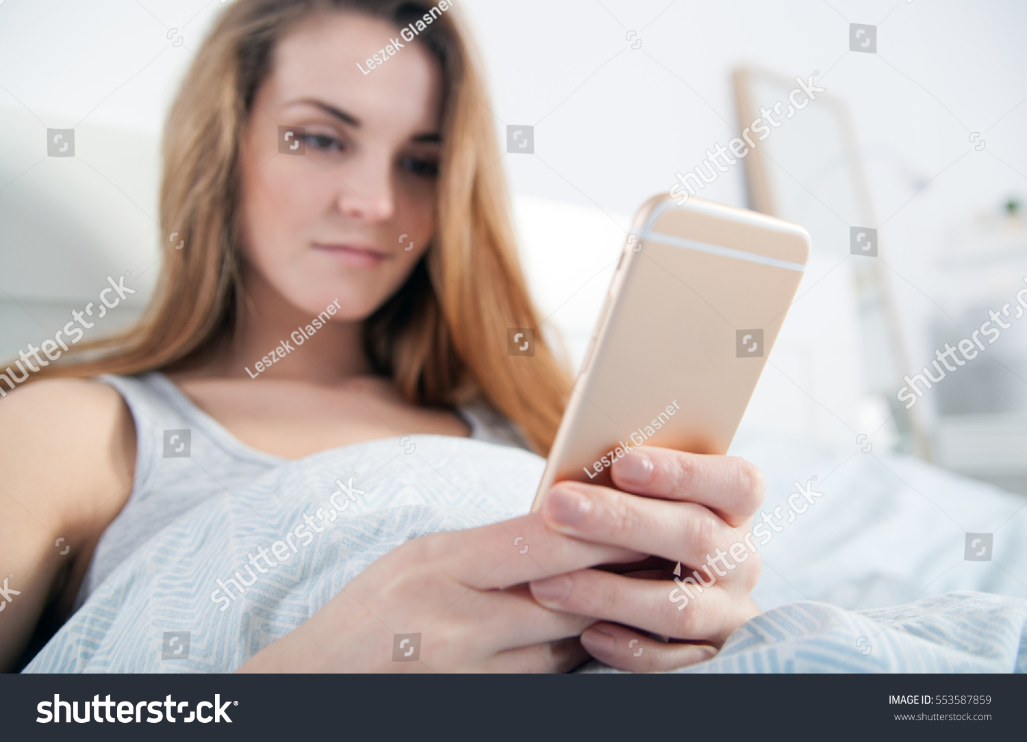 Young woman checking her smart phone lying in bed #553587859
