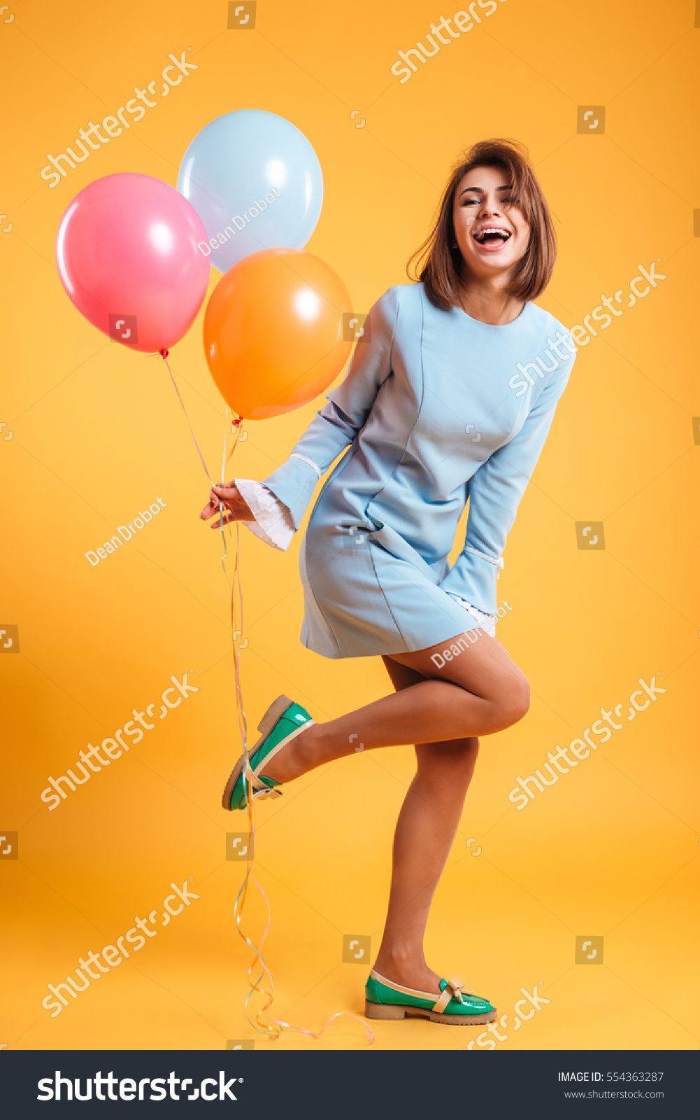 Full length of cheerful young woman with balloons standing and laughing #554363287