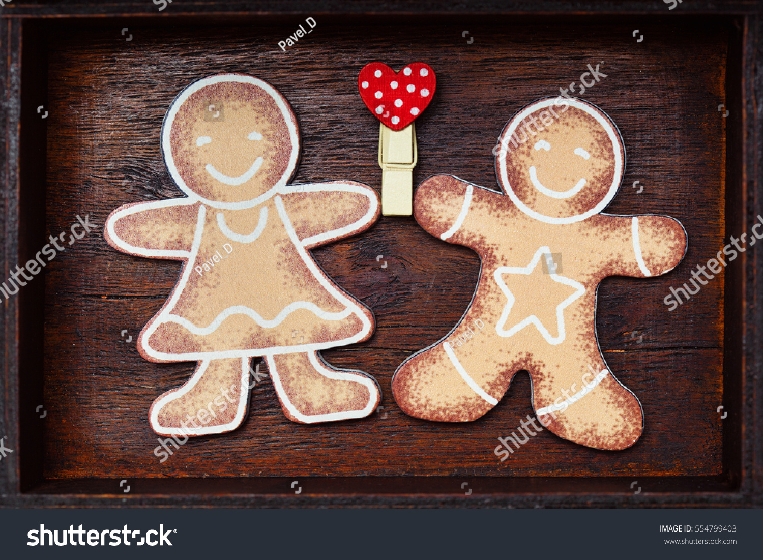 Valentine's Day. Lovers gingerbread men holding red heart (love symbol) on wooden background. #554799403