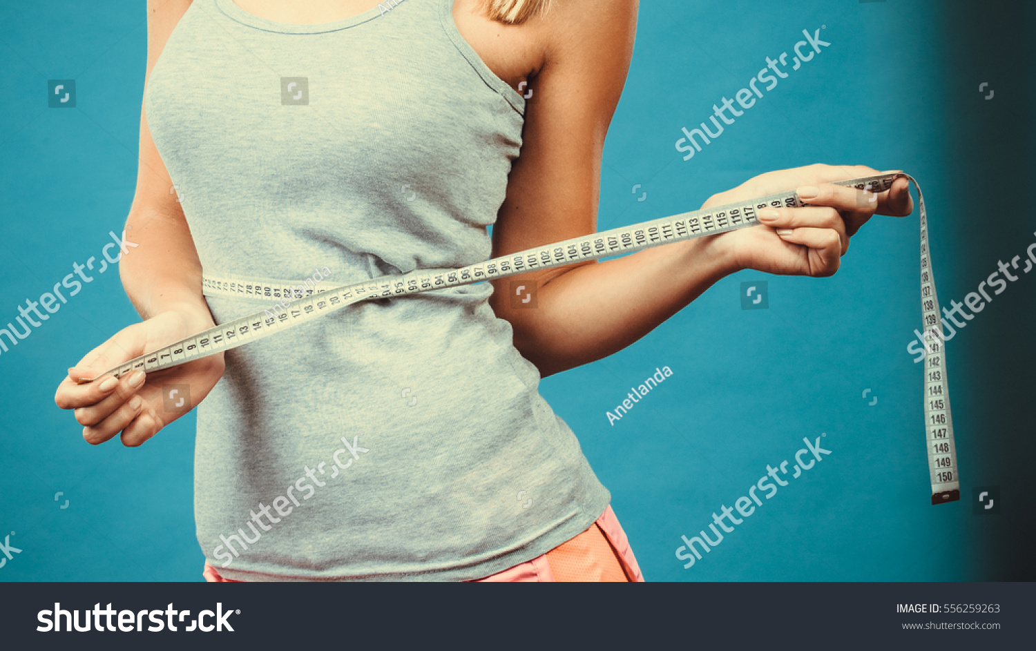 Weight loss, slim body, healthy lifestyle concept. Fit fitness girl measuring her waistline with measure tape on blue #556259263