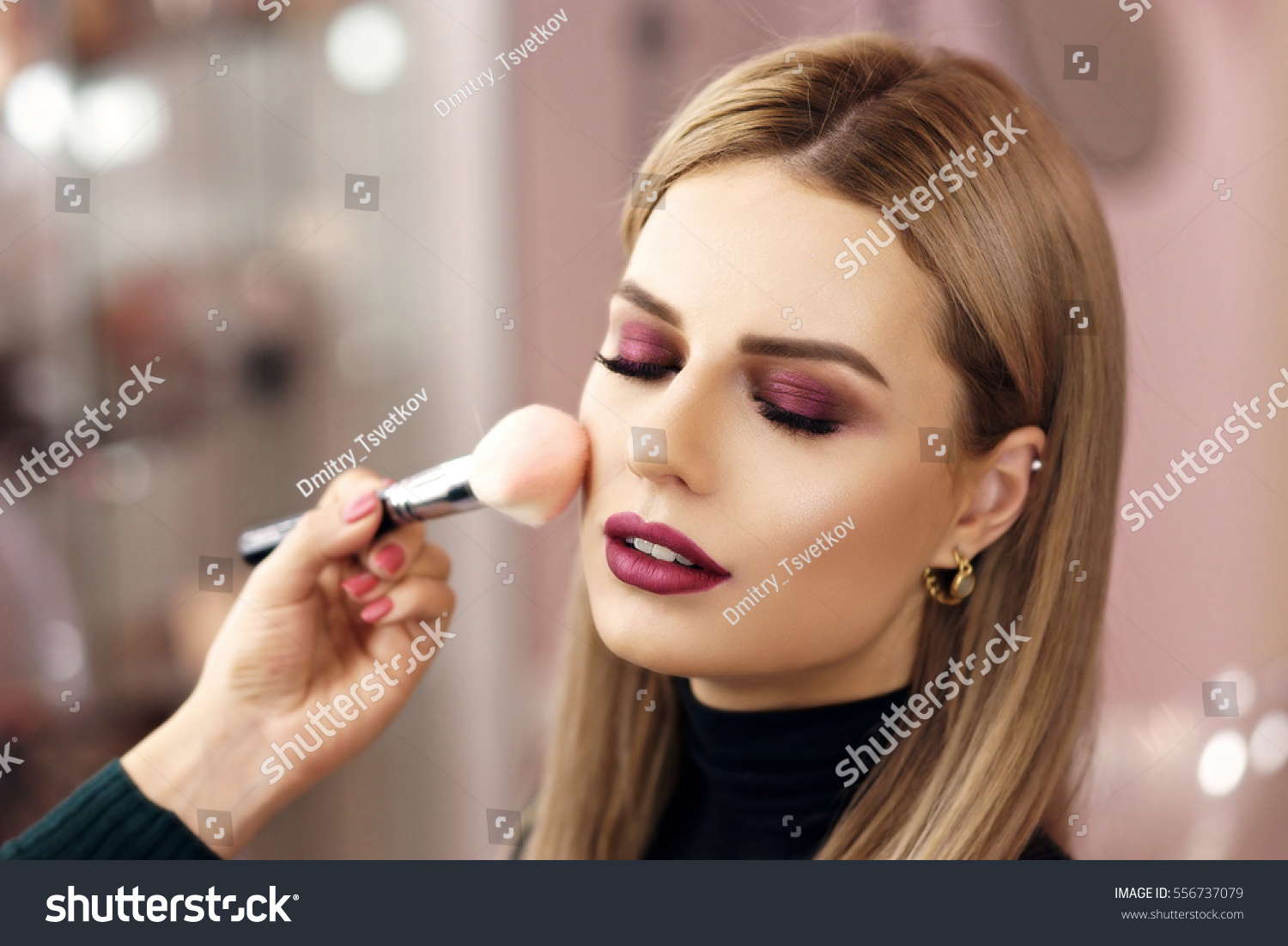 Process of making makeup. Make-up artist working with brush on model face. Portrait of young blonde woman in beauty saloon interior. Applying tone to skin. #556737079