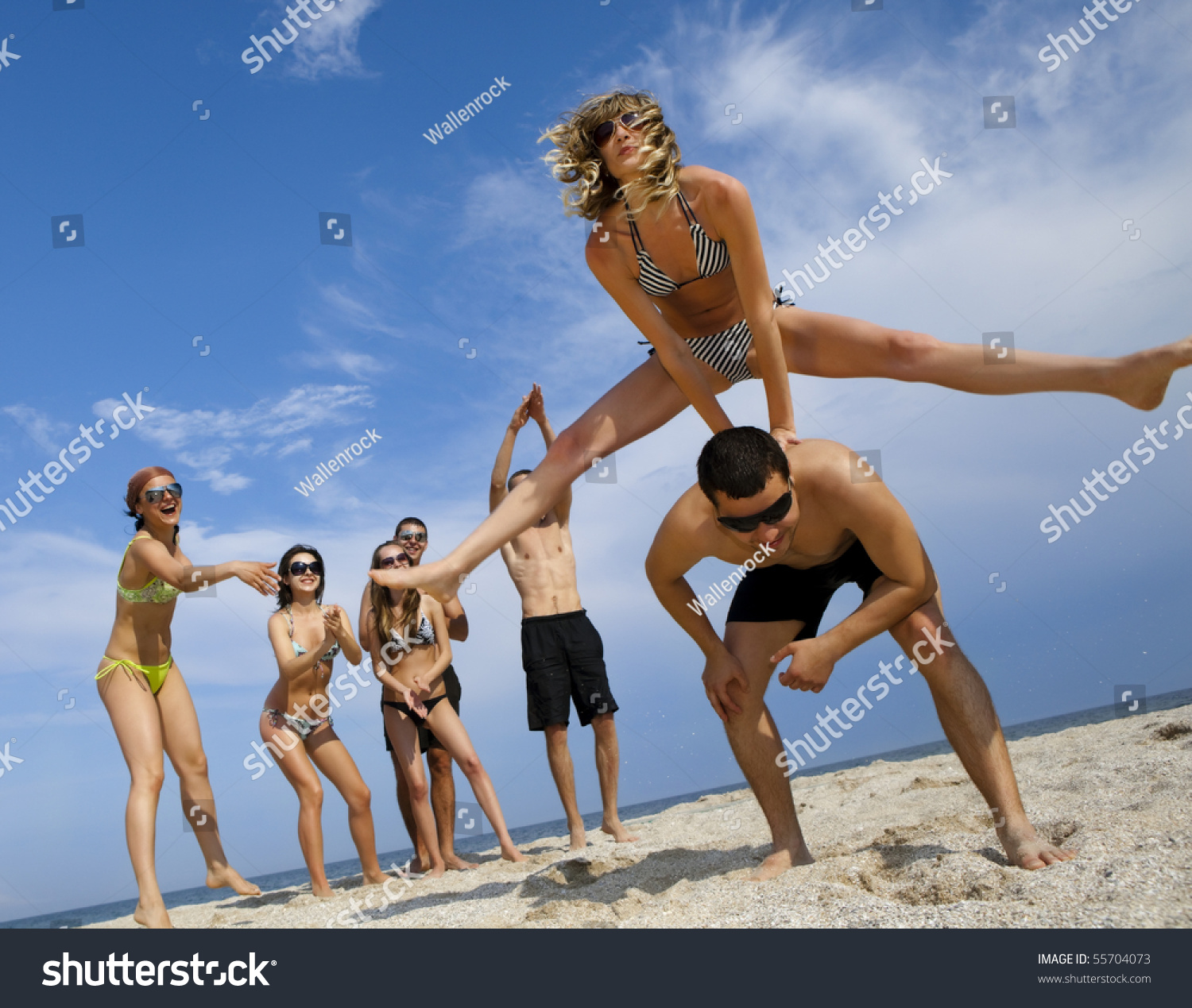 Young girl to jump across her boyfriend against joyful team of friends having fun at the beach #55704073