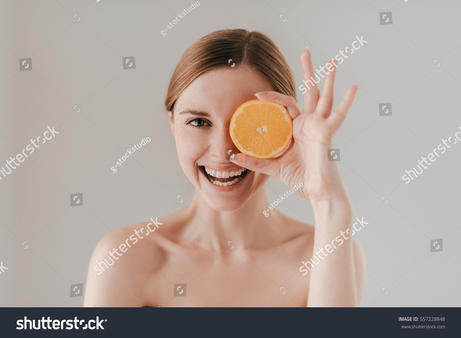 Healthy eating makes you beautiful. Attractive young woman with freckles on face holding orange slice and smiling while standing against background #557228848