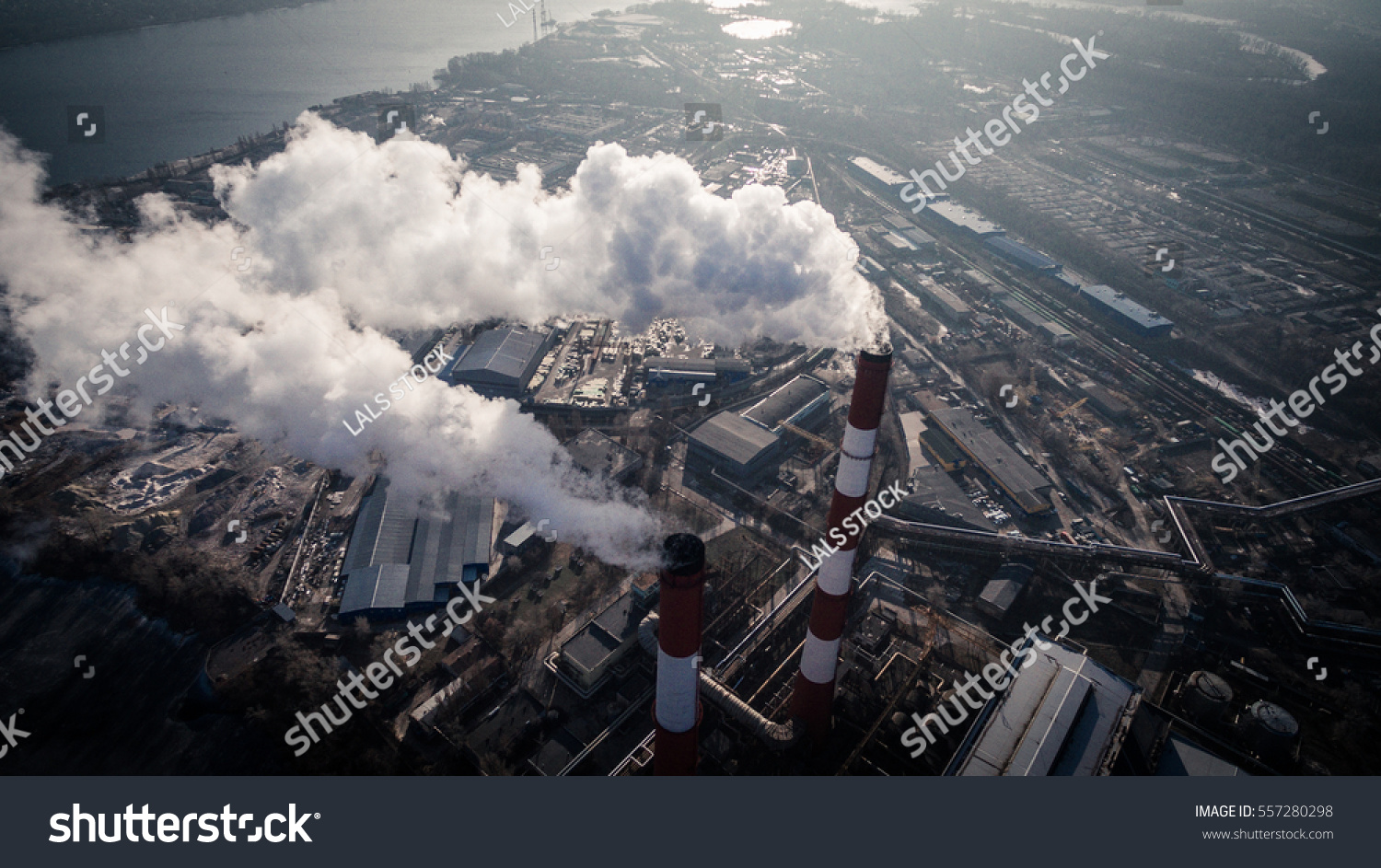 Air pollution by smoke coming out of two factory chimneys. Industrial zone in the city. Kiev, Ukraine, aerial view #557280298