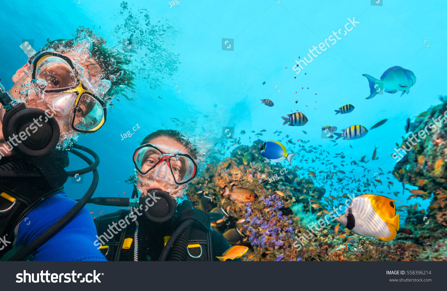 Couple of scuba divers looking at camera underwater. Beautiful coral reef with many fish on background #558396214