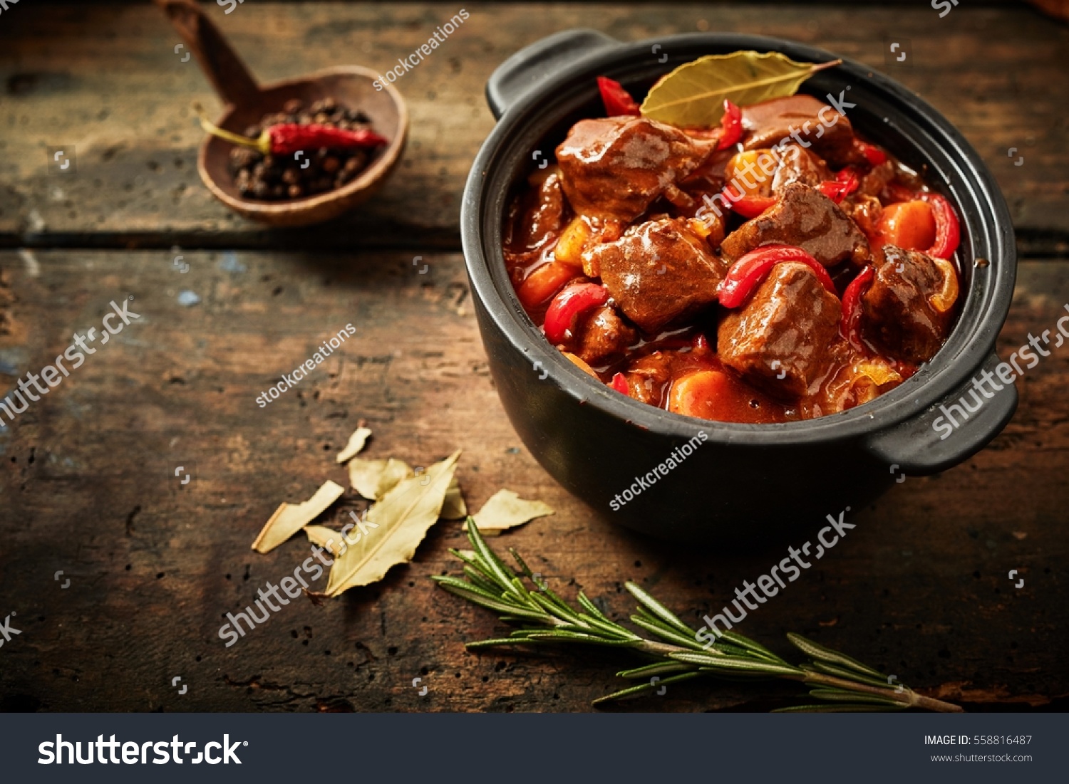 Pot of hungarian goulash on rustic wood background with chili peppers and laurel and copy space #558816487