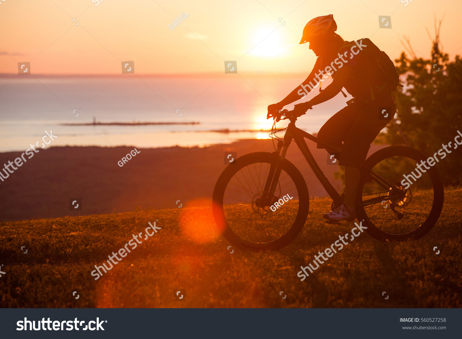 A woman riders he mountain bike trail on single track trail above a lake at sunset #560527258