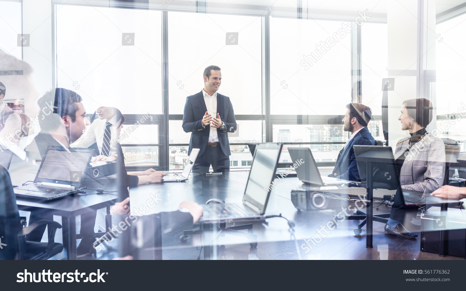 Successful team leader and business owner leading informal in-house business meeting. Businessman working on laptop in foreground. Business and entrepreneurship concept. #561776362