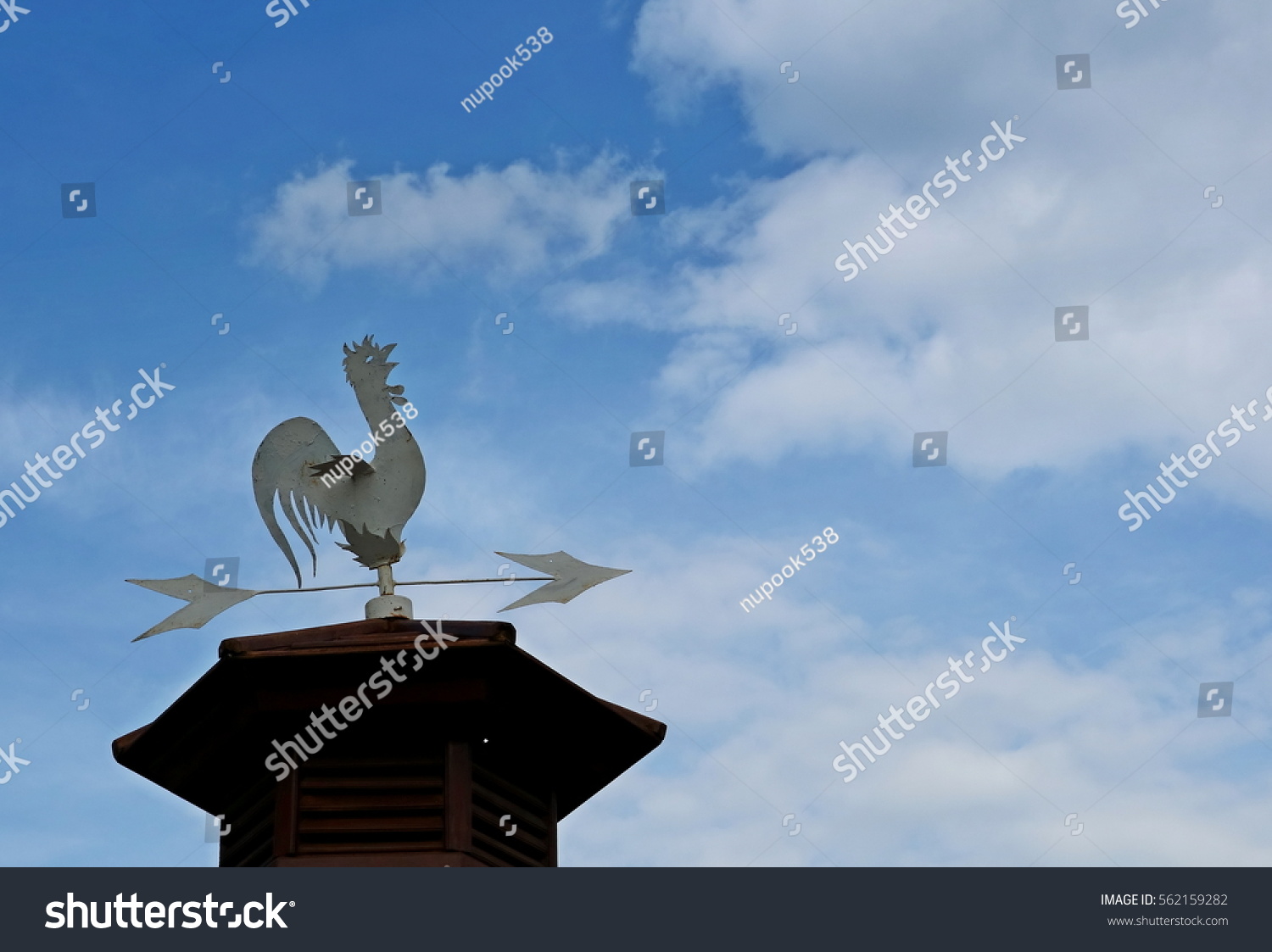 An old chicken metal weather vane, or weathercock on top roof with beautiful blue sky with white cloud and copy space #562159282