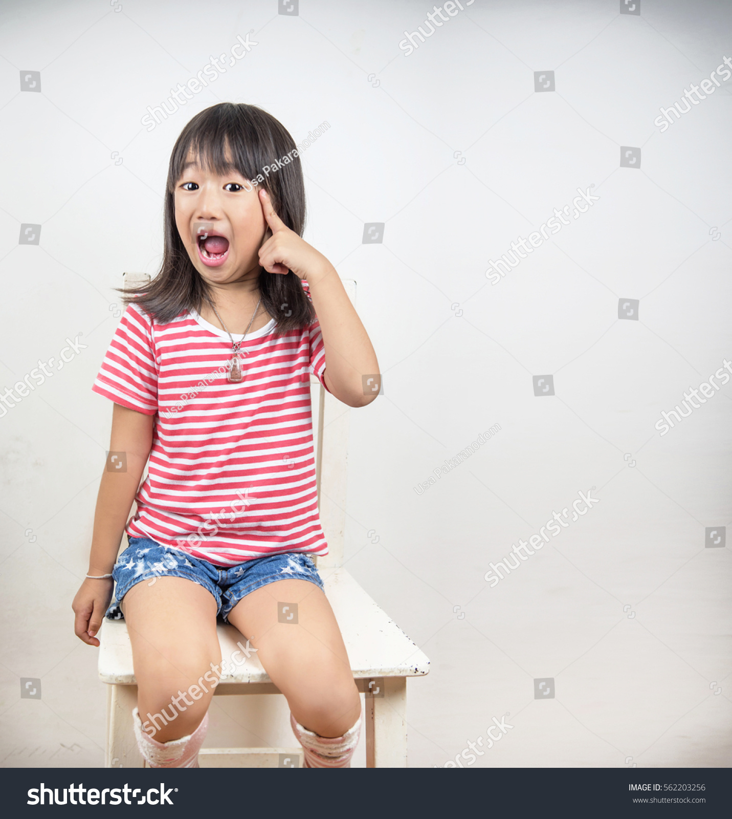 Clever little girl Asian with a bright idea pointing upwards with her finger to gain attention Isolated on white with blank copyspace above her finger #562203256