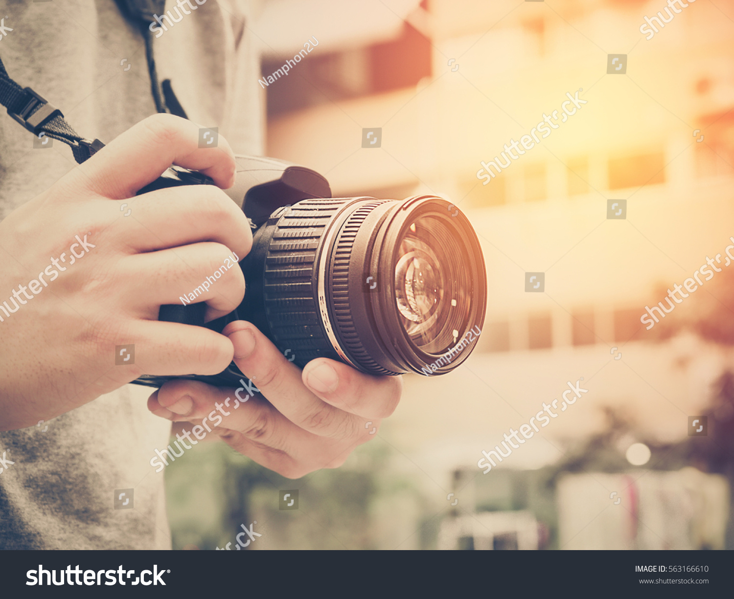 Photography or traveler Concept.The photographer hold DSRL camera in his hands with cityscape blur background and sunlight in summer time, selective focus. Photo of Vintage and filtered process. #563166610