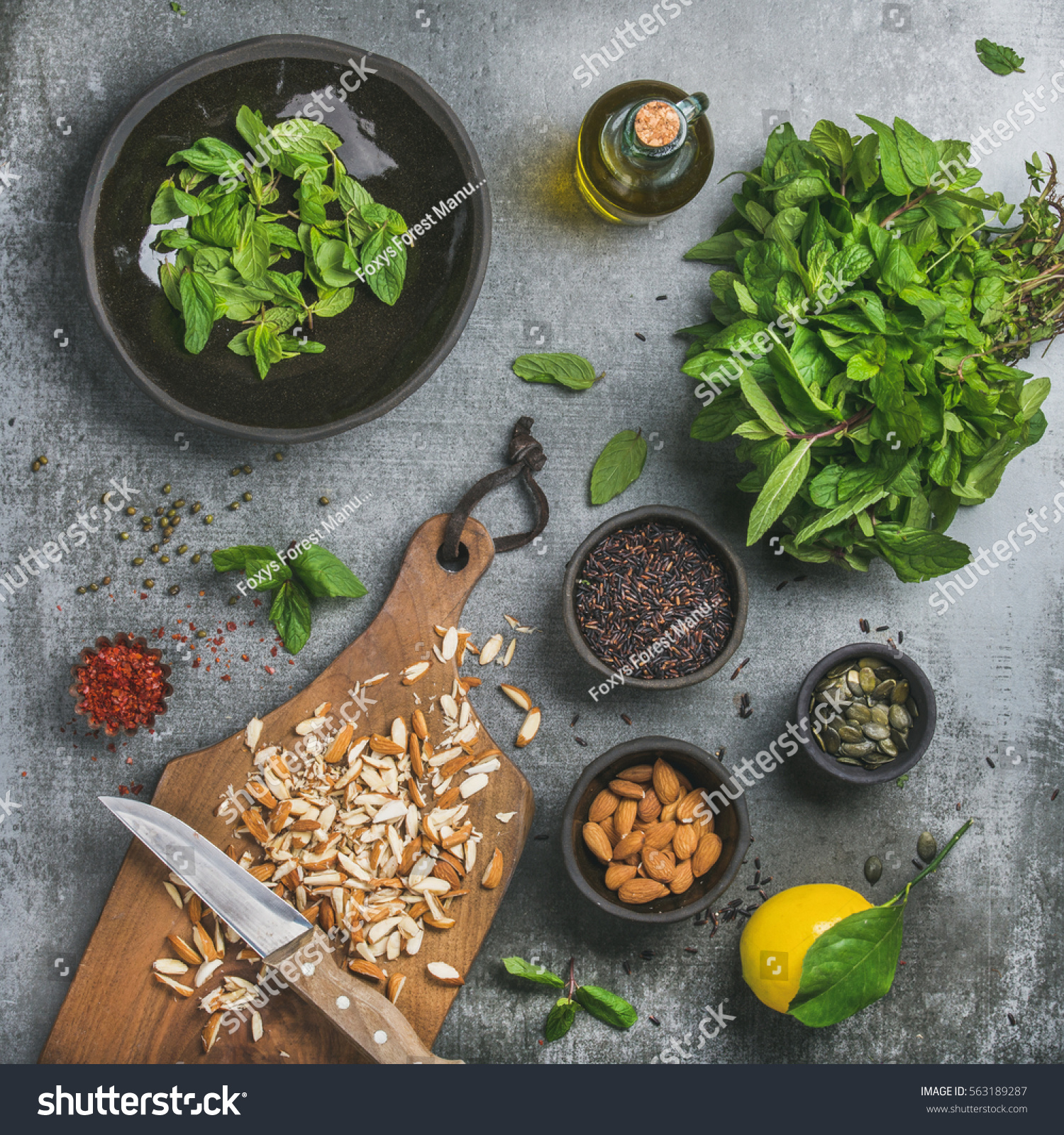 Healthy, vegan, clean eating cooking ingredients. Chopped almond, fresh mint, oil, black rice, pumpkin seed, spices, lemon over grey concrete background, top view, square crop Detox or dieting concept #563189287