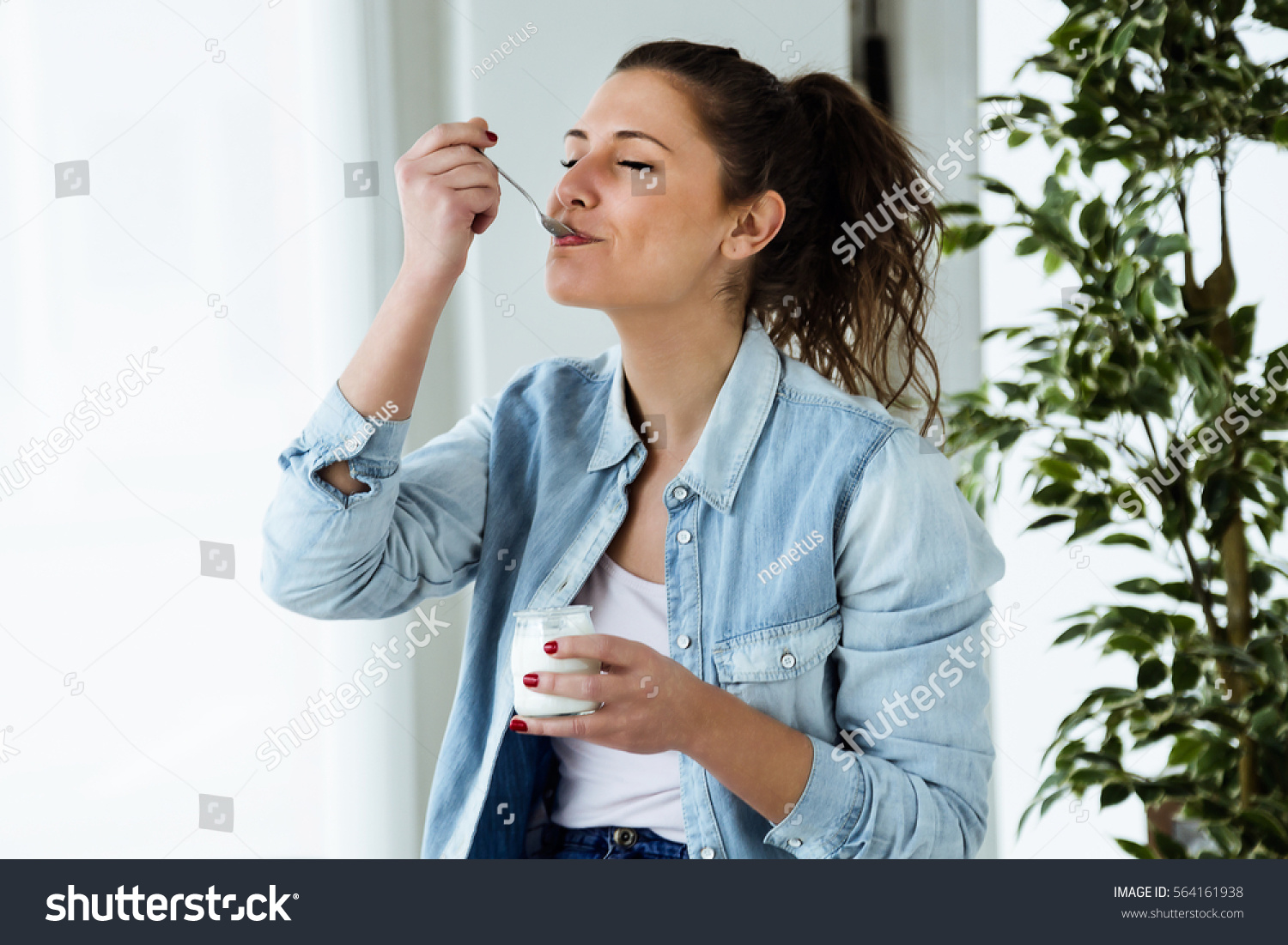 Portrait of beautiful young woman eating yogurt at home. #564161938