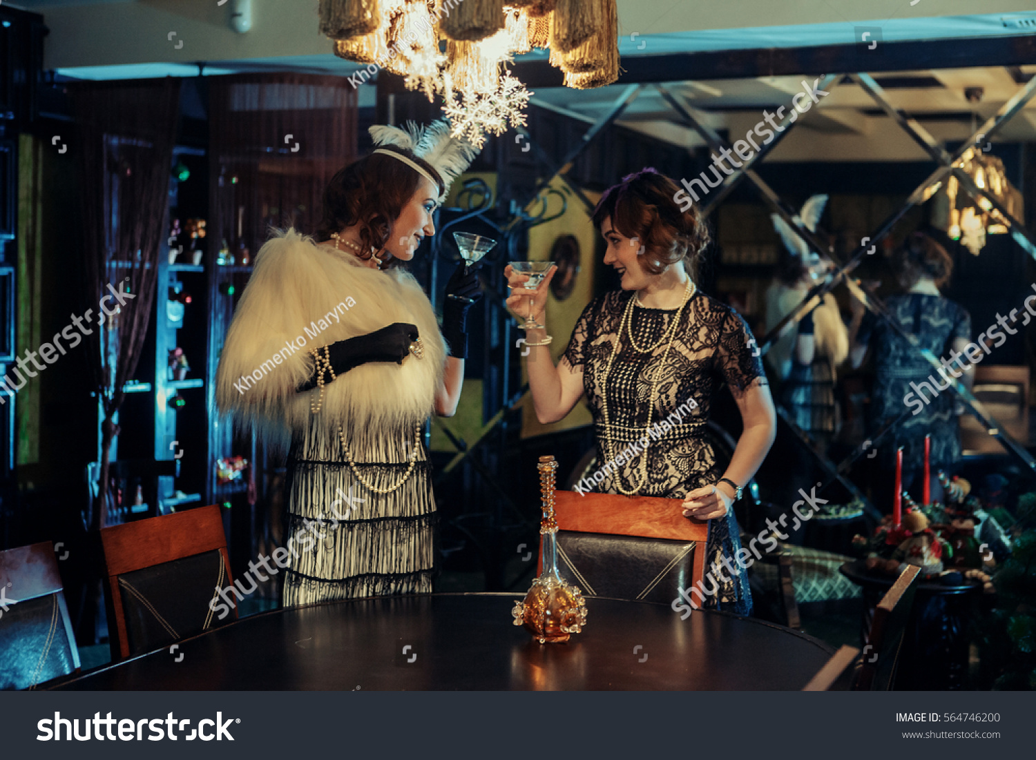 20s style concept. Two pretty ladies in vintage dresses dancing and drinking in old-fashioned interior. Having fun  #564746200