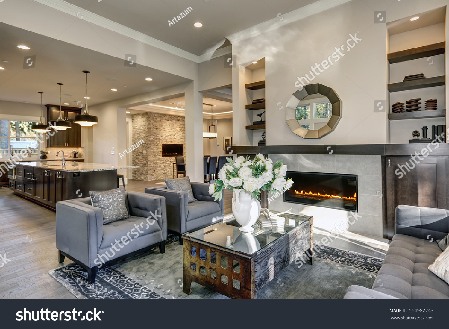 Chic living room filled with built-in cabinets flanking round mirror atop grey tile fireplace, tufted sofa facing two armchairs and window wall overlooking  lush outdoors. Northwest, USA #564982243