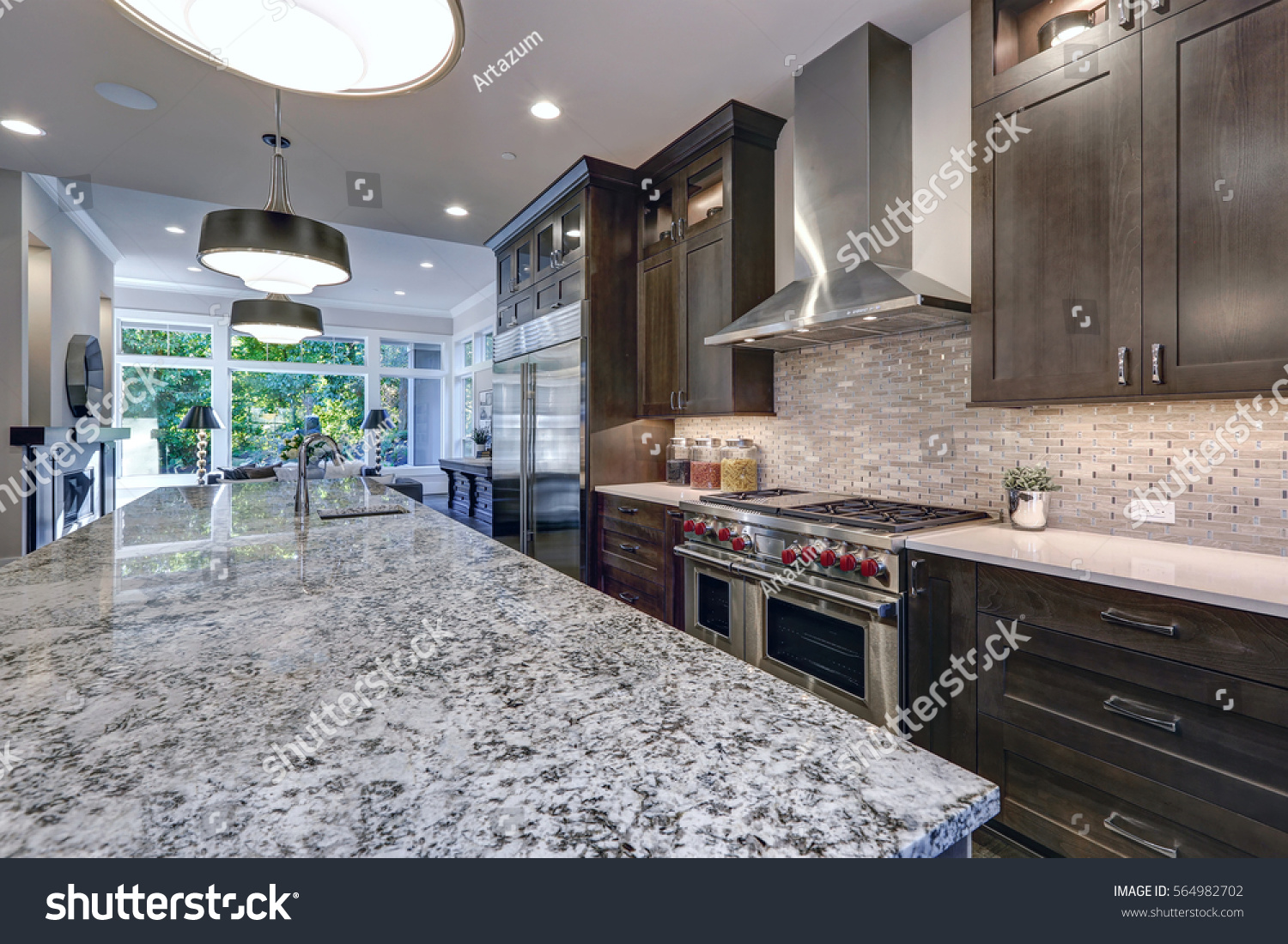 Modern kitchen with brown kitchen cabinets, oversized kitchen island, granite countertops, stainless steel hood over six burner Range and beige backsplash. Northwest, USA
 #564982702