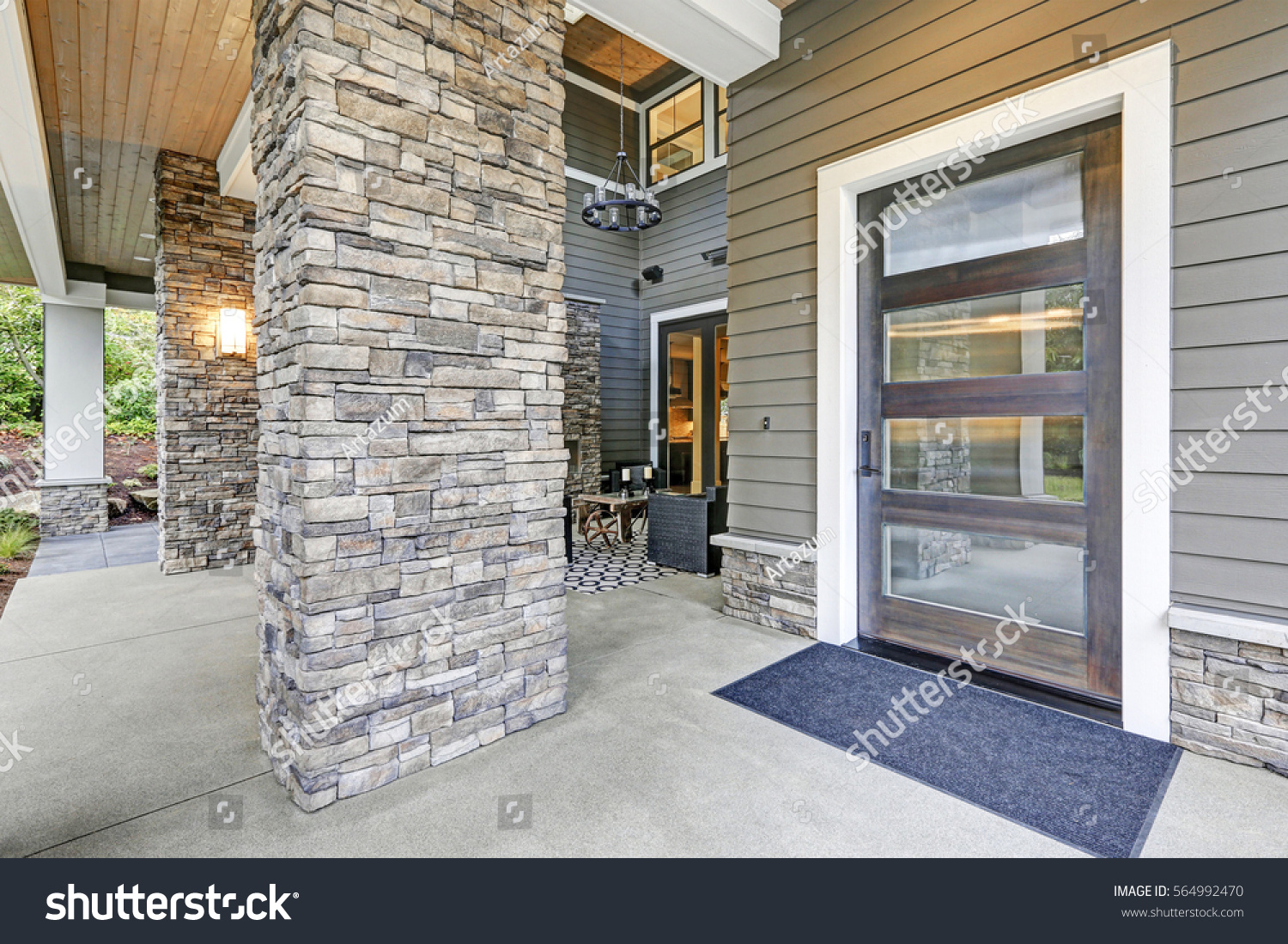 Covered porch accented with stone column and modern glass front door. Northwest, UISA #564992470