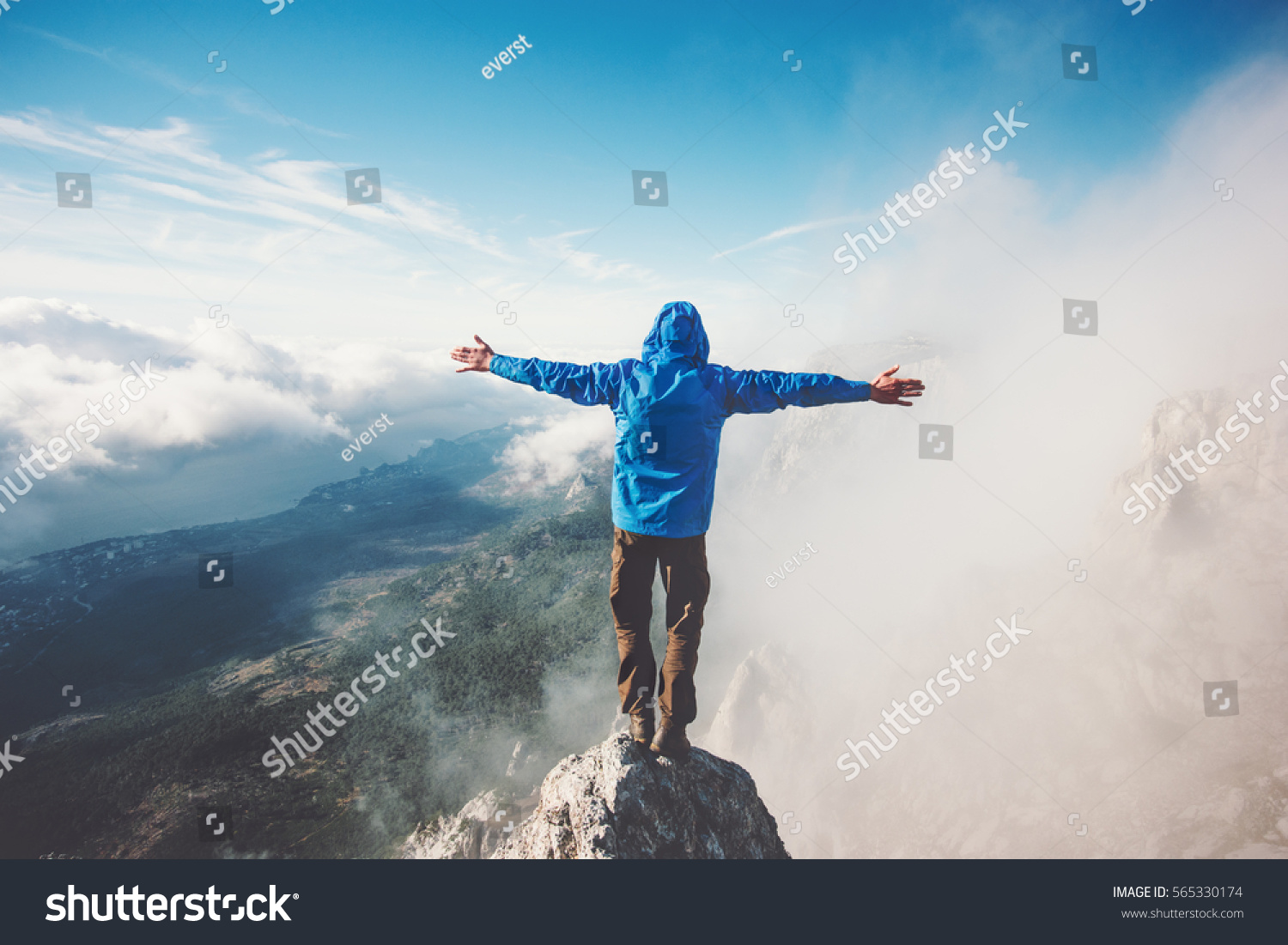 Happy Man on mountain summit enjoying aerial view hands raised over clouds Travel Lifestyle success concept adventure active vacations outdoor freedom emotions #565330174