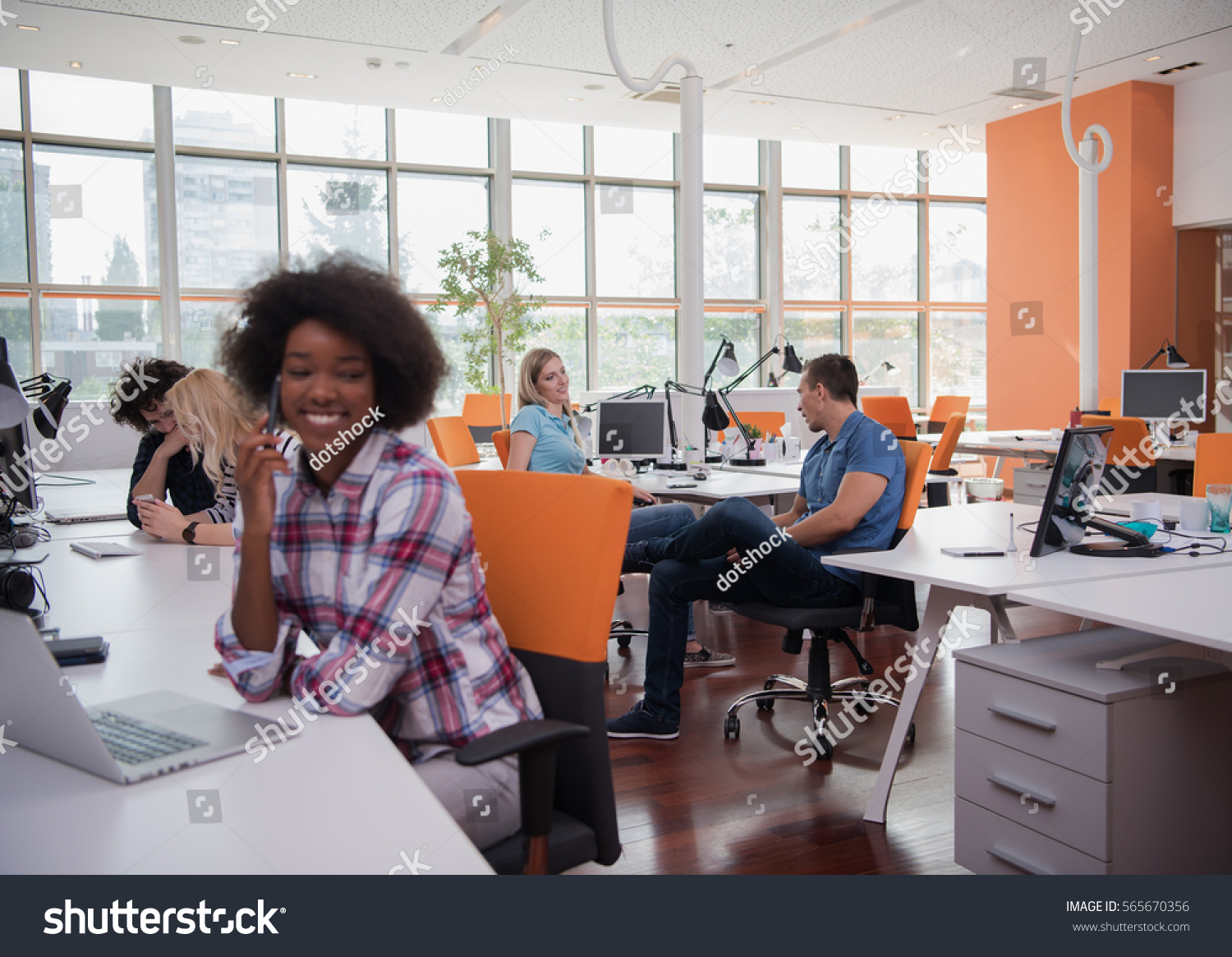young smiling African American informal businesswoman working in the office with colleagues in the background #565670356