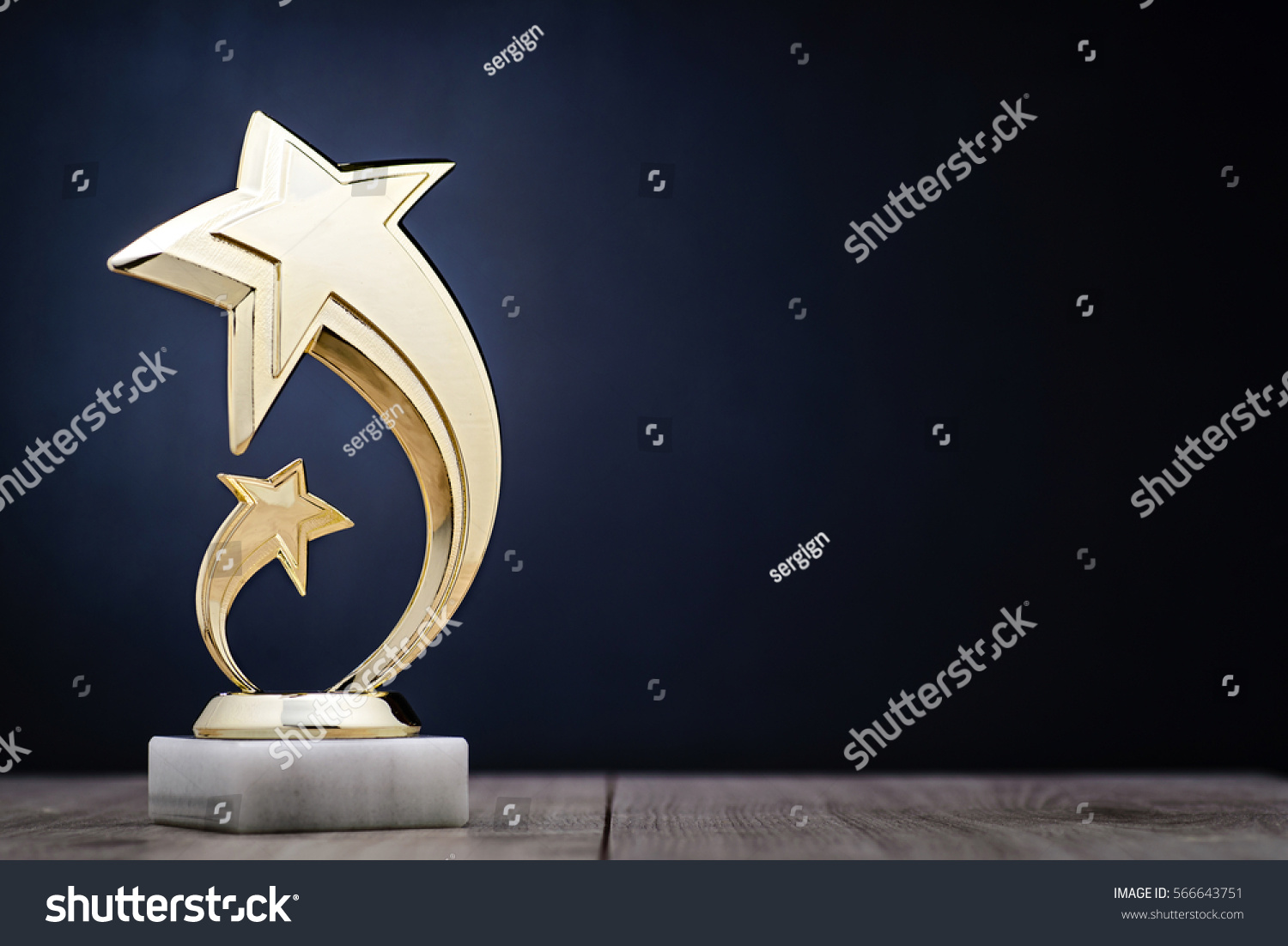 Elegant gold winners trophy with shooting stars to be awarded for the first place in a competition or championship over a dark blue background with copy space #566643751