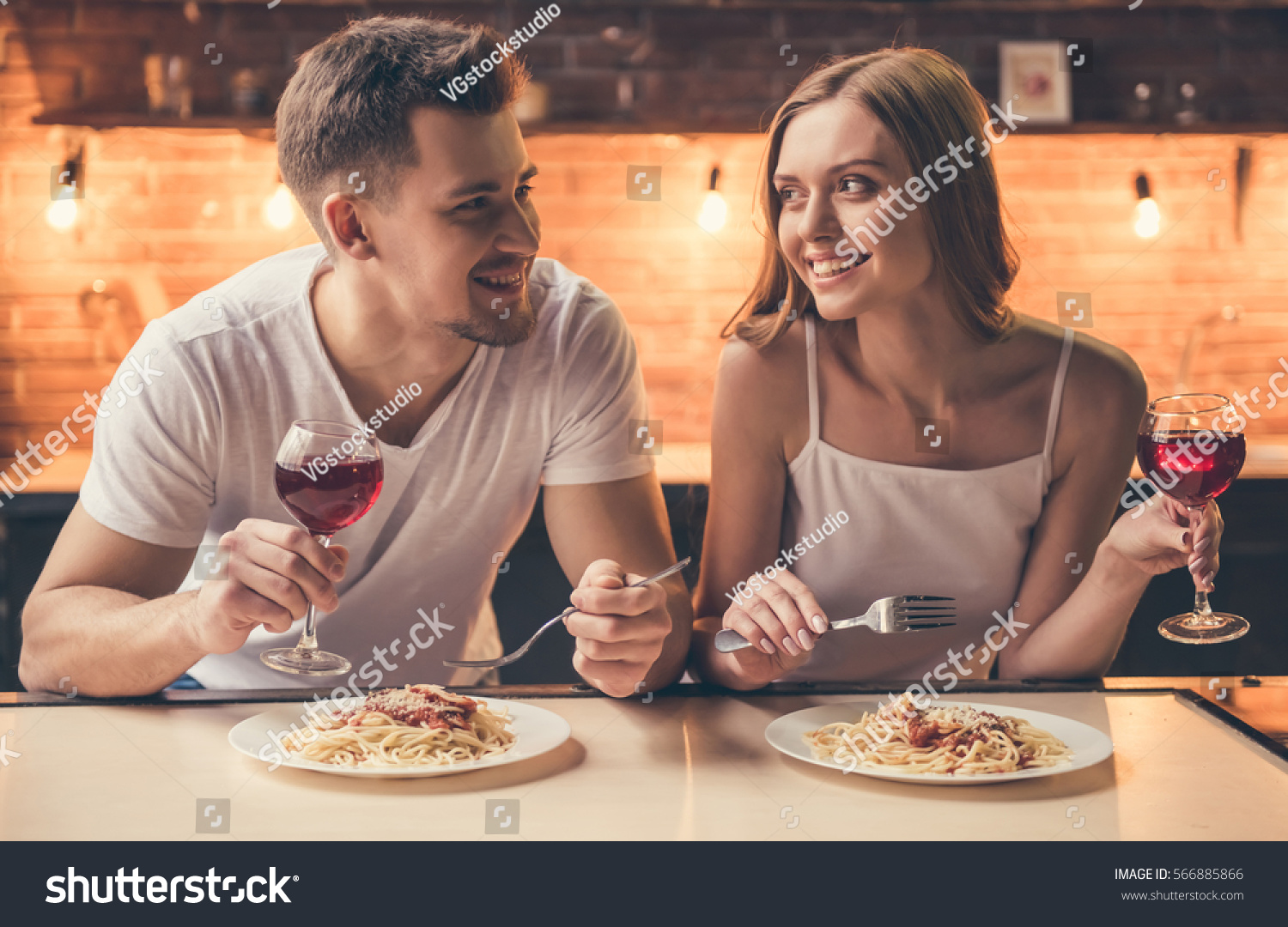Beautiful couple is talking and smiling while having a romantic dinner together in the kitchen #566885866