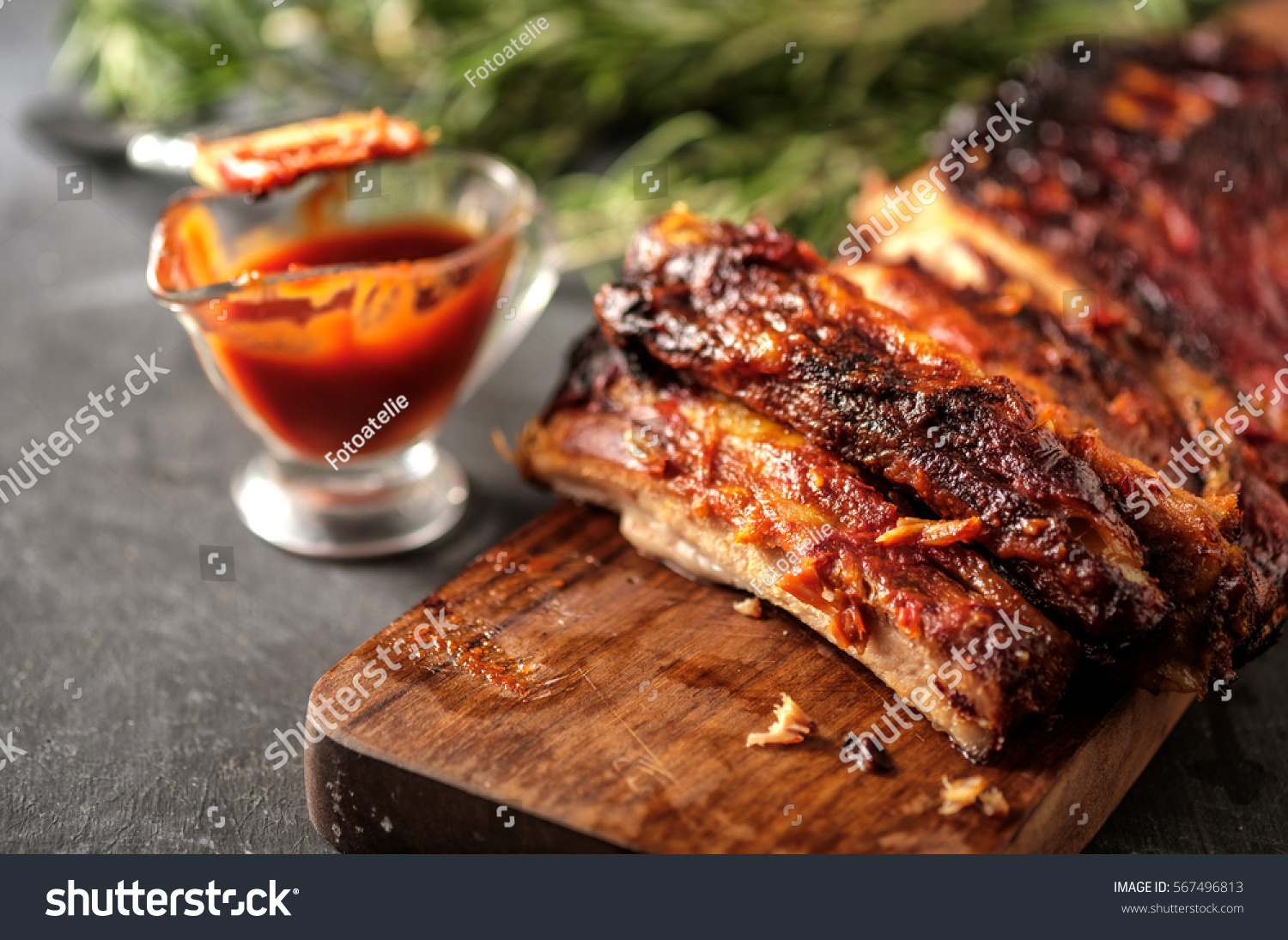 Delicious barbecued ribs seasoned with a spicy basting sauce and served with chopped fresh vegetables on an old rustic wooden chopping board in a country kitchen #567496813