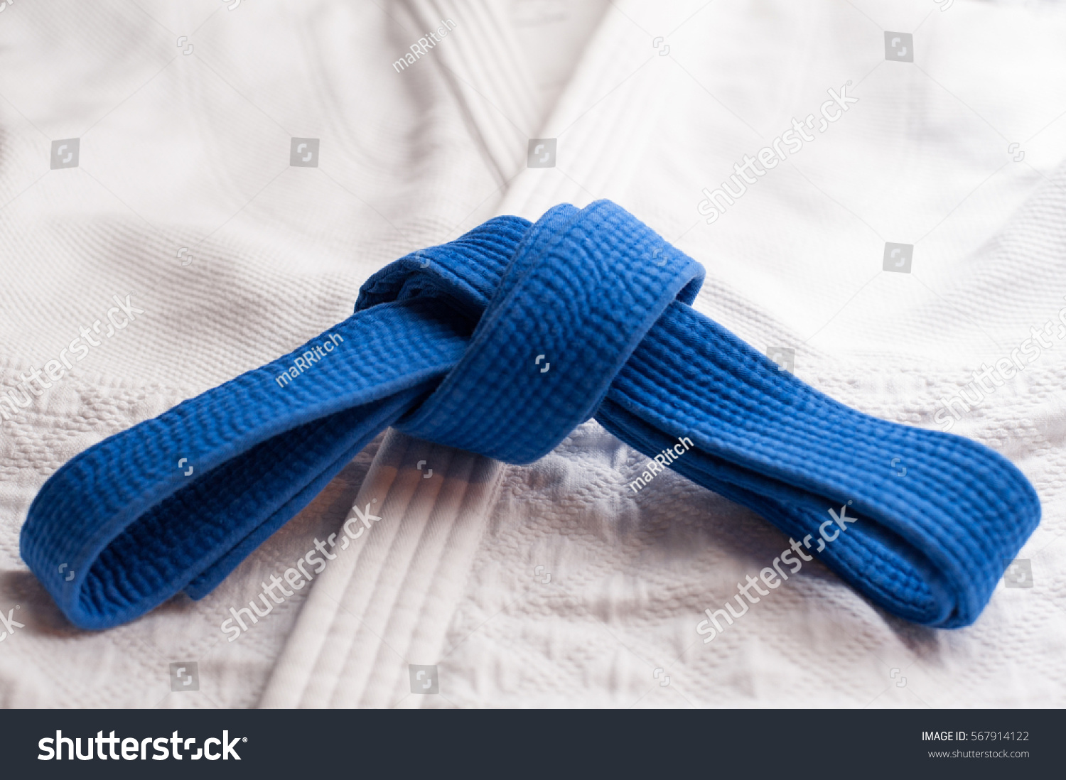 Blue judo, aikido or karate belt tied in a knot with white kimono in background #567914122