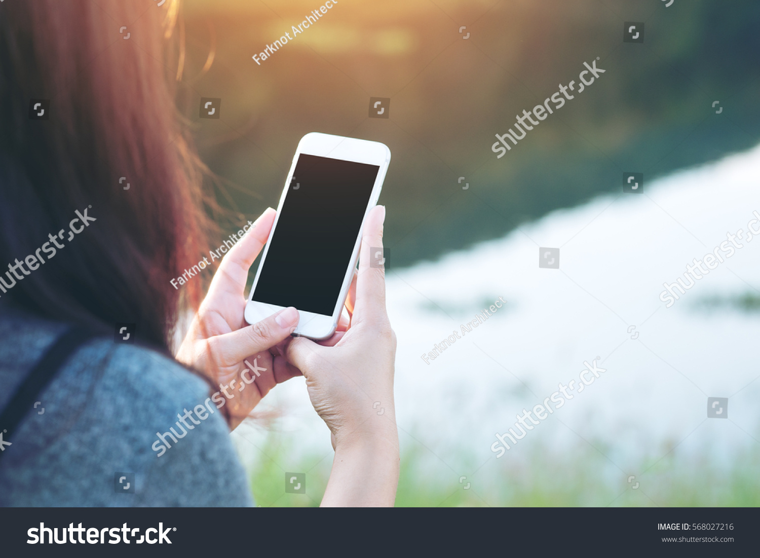 Mockup image of a woman using smart phone with blank black screen at outdoor and lake nature background #568027216