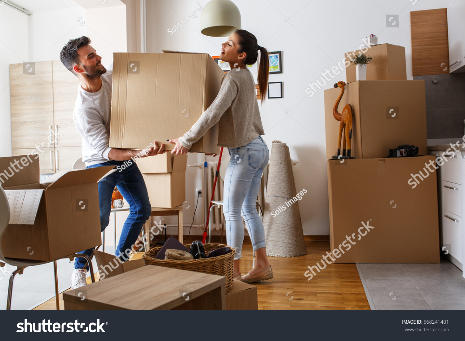 Young couple carrying big cardboard box at new home.Moving house. #568241401