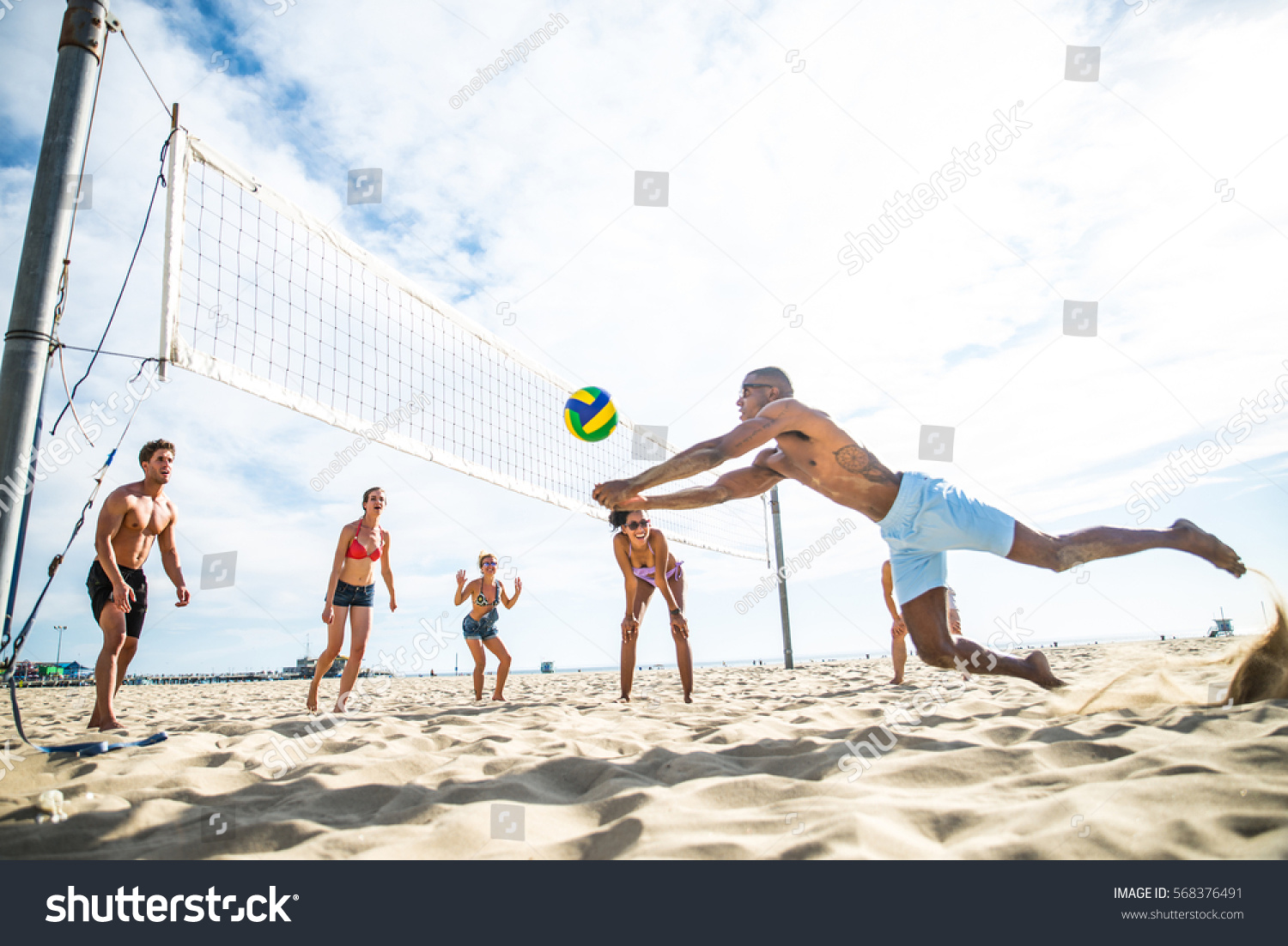 Group of friends playing beach volley - Multi-ethic group of people having fun on the beach #568376491