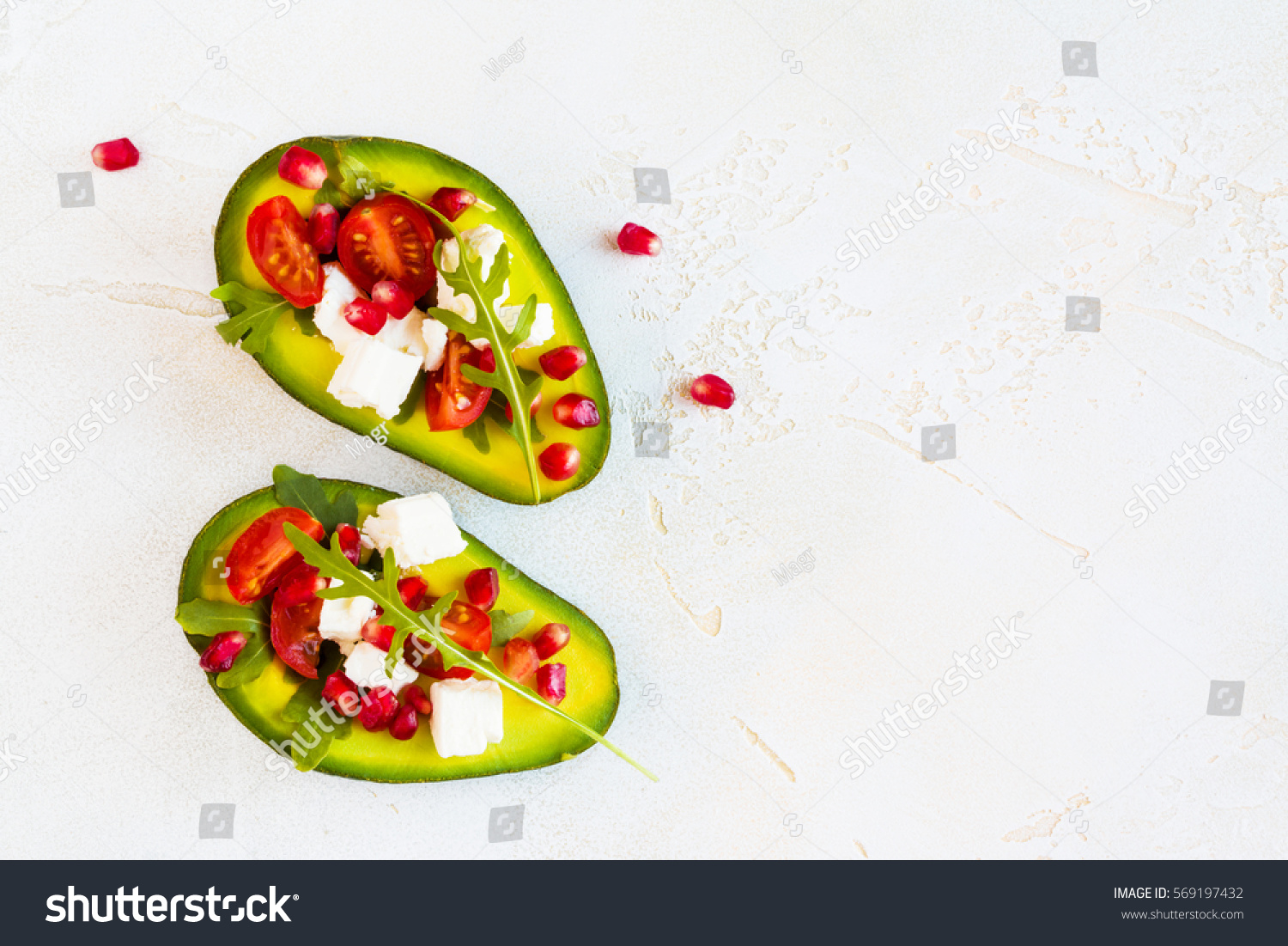 Healthy organic vegetarian diet food, avocado with pomegranate seeds, feta cheese, arugula leaves and cherry tomatoes on the table, top view. #569197432
