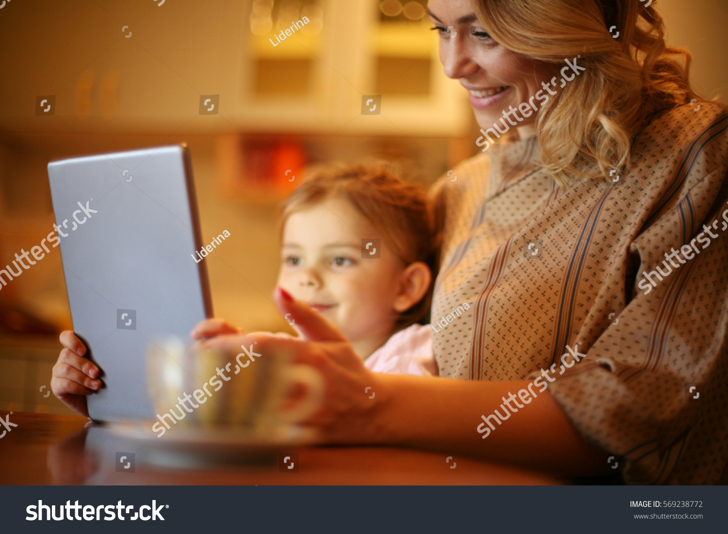 Pretty blonde Caucasian girl reading with her mother from tablet and smiling. Focus on woman. #569238772