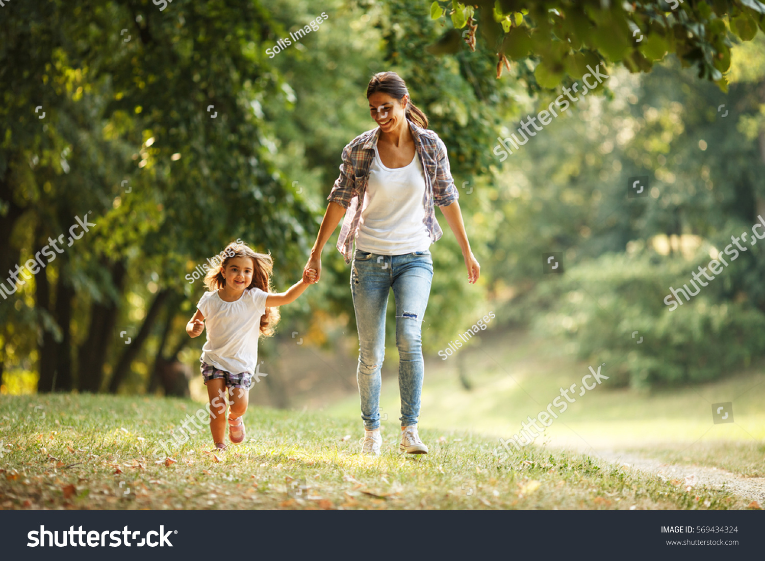 Mother and daughter playing and running around the park on beautiful morning. #569434324