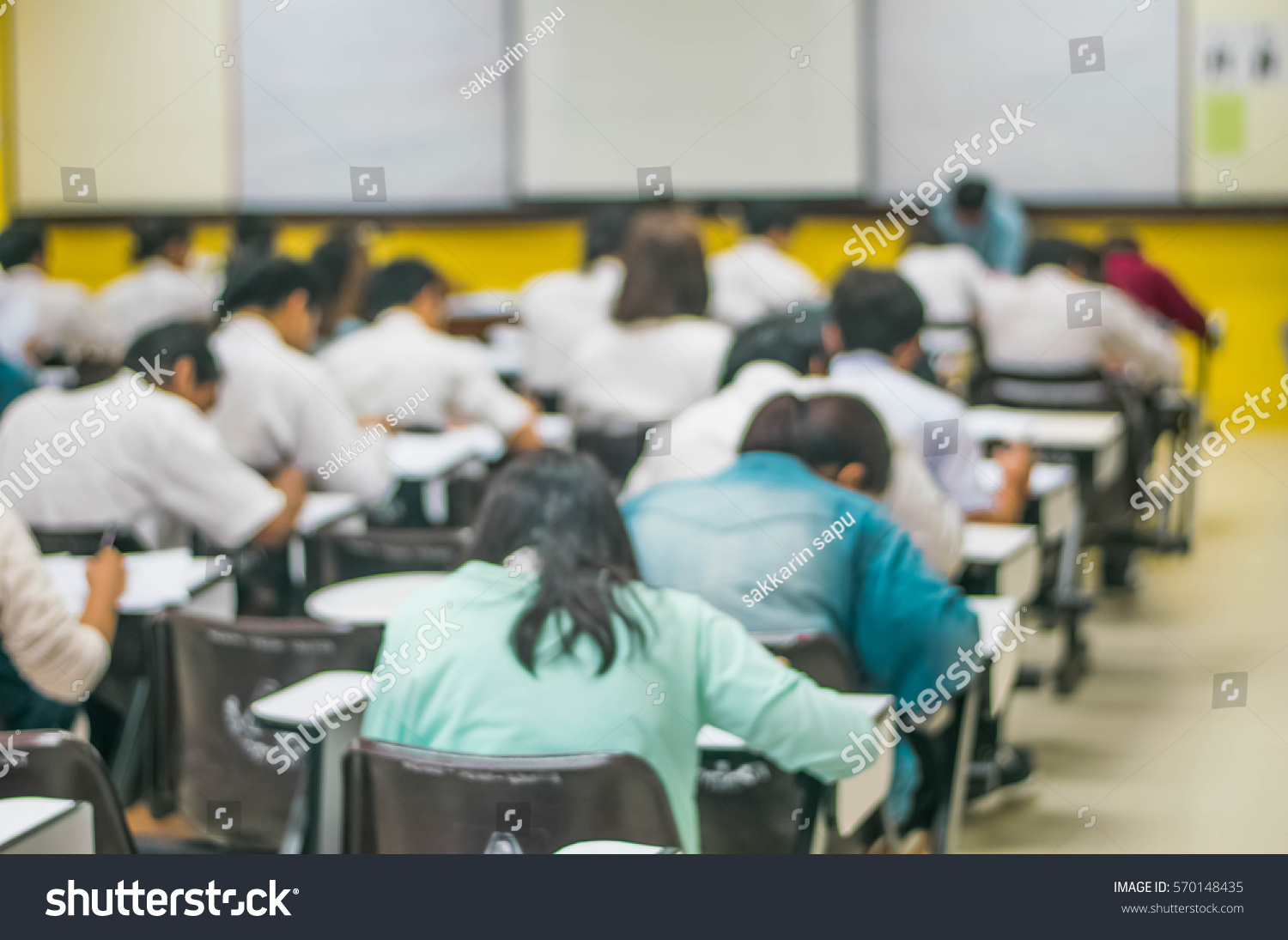 Blur abstract background of examination room with undergraduate students inside. Blurred view of student doing final test in exam hall. Blurry view of study chairs in classroom of university or campus #570148435