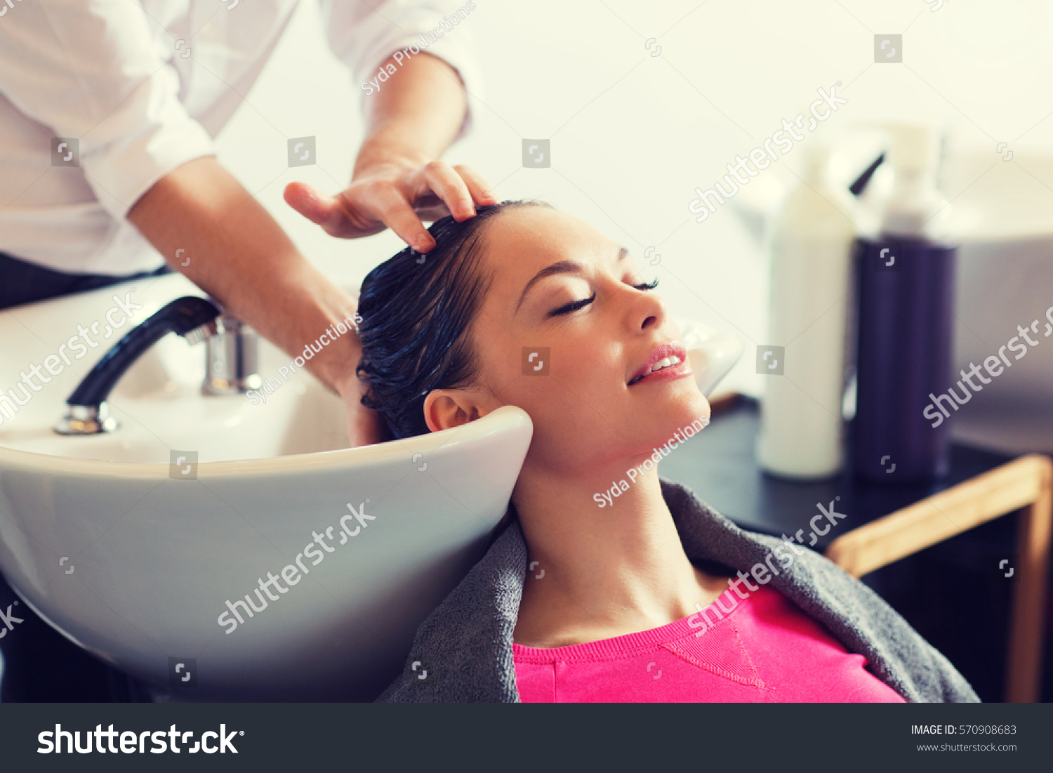 beauty and people concept - happy young woman with hairdresser washing head at hair salon #570908683