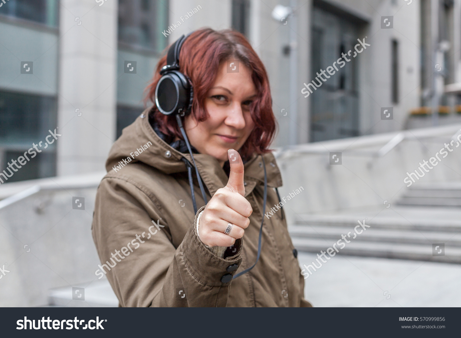 Happy young red-haired woman with big headphones shows thumb up #570999856