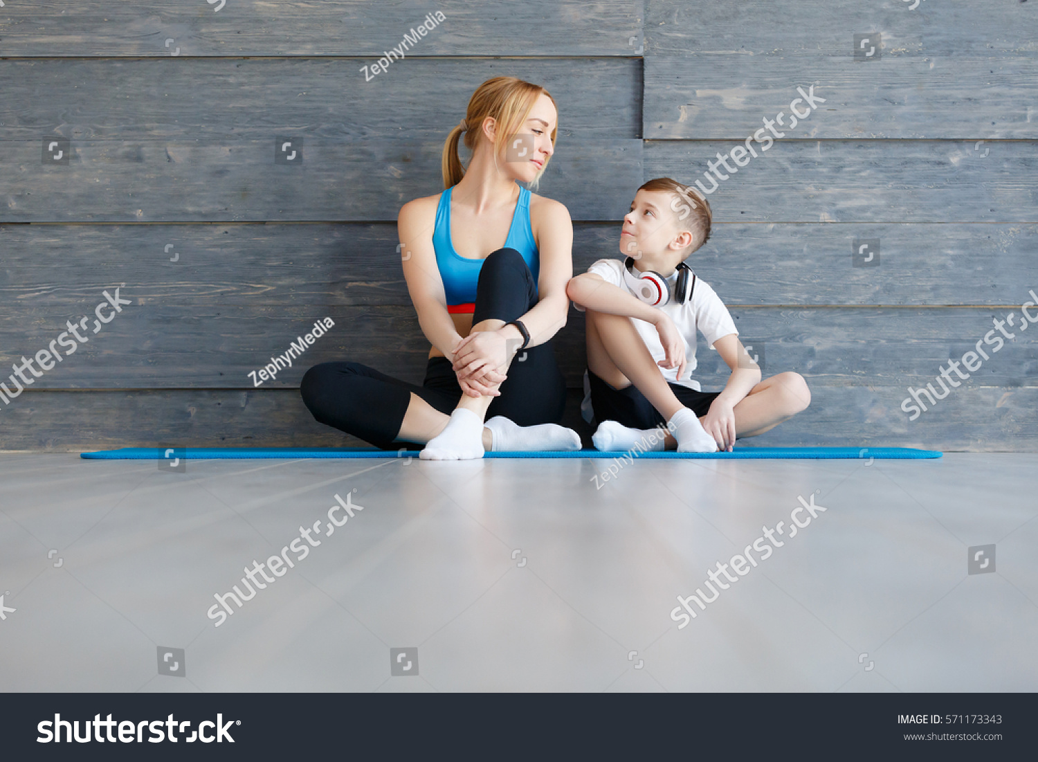 Fitness mother with her 9 years old son. Sports mom with kid relaxing after morning work-out at home. Mum and child do the exercises together, healthy family lifestyle concept #571173343
