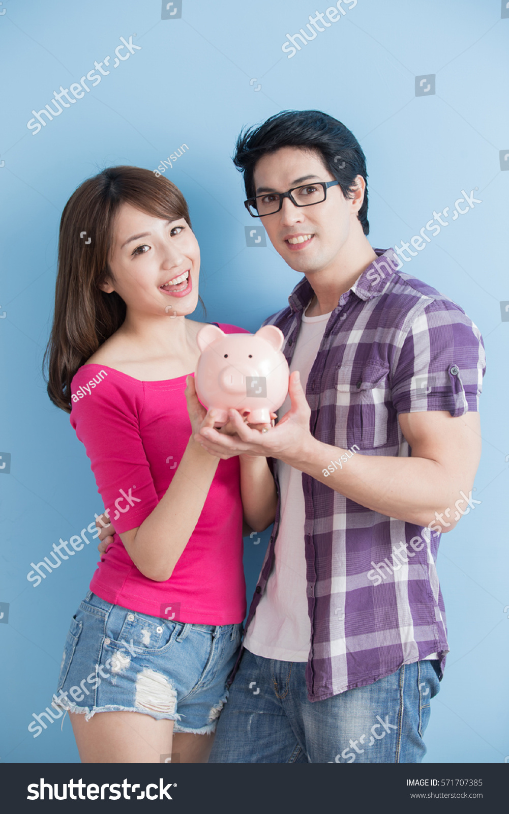 young couple hold pink pig bank and smile happily isolated on blue background #571707385