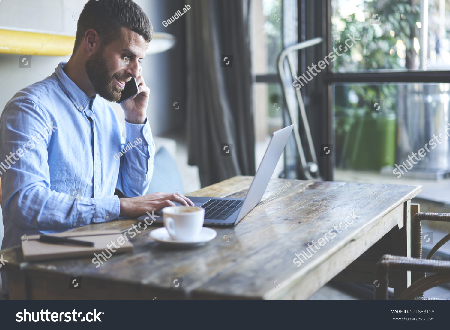 Successful male owner of business company talking with operator while making banking online consulting about cash remittance paying for bills using wireless internet and modern laptop in cabinet #571883158