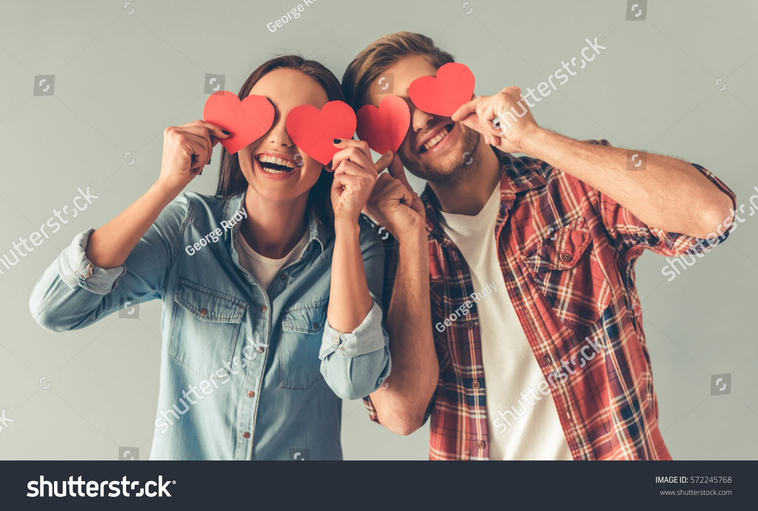 Happy young couple is holding red paper hearts and smiling, on gray background #572245768