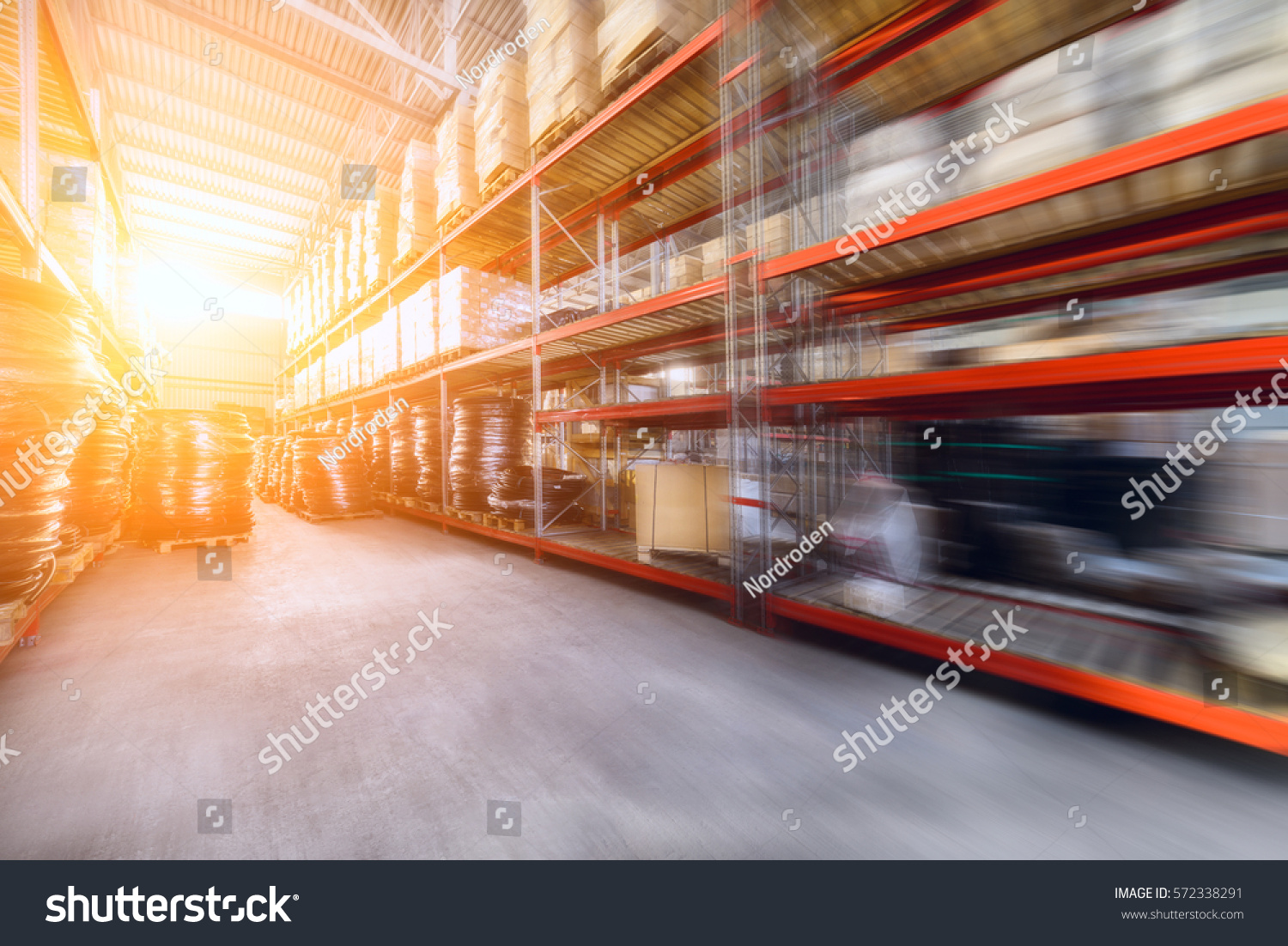 Warehouse industrial and logistics companies. Commercial warehouse. Boxes and crates stocked on the shelves of three storey. The effect of motion blur. Bright sunlight. #572338291