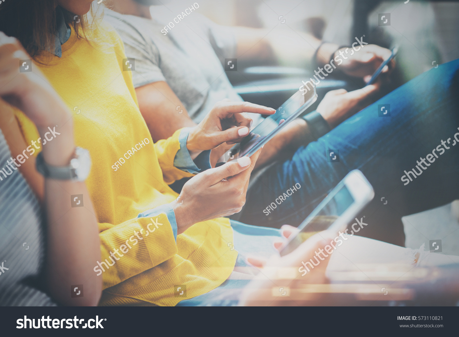 Group of young hipsters sitting on sofa holding en hands and using digital tablet,smartphone.Coworking team concept.Horizontal,blurred background #573110821