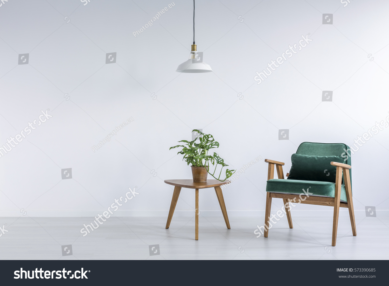 White room with green armchair, small table and plant #573390685