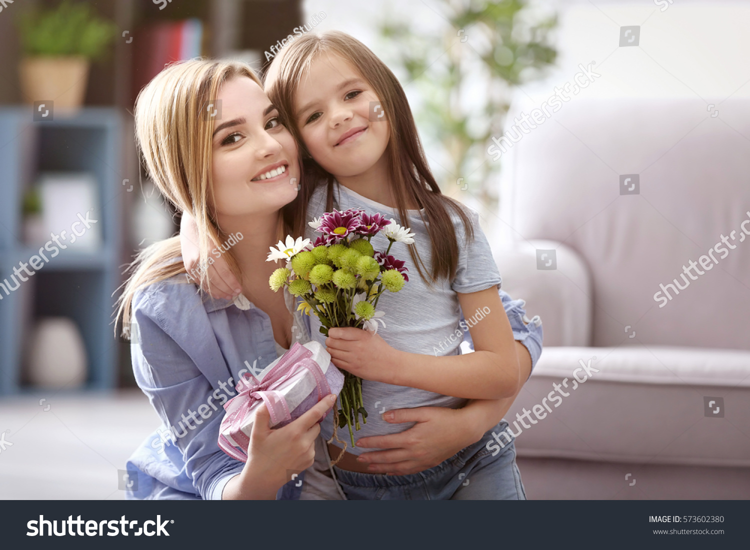 Beautiful young woman with present and bouquet of flowers from her daughter. Mother's day concept #573602380