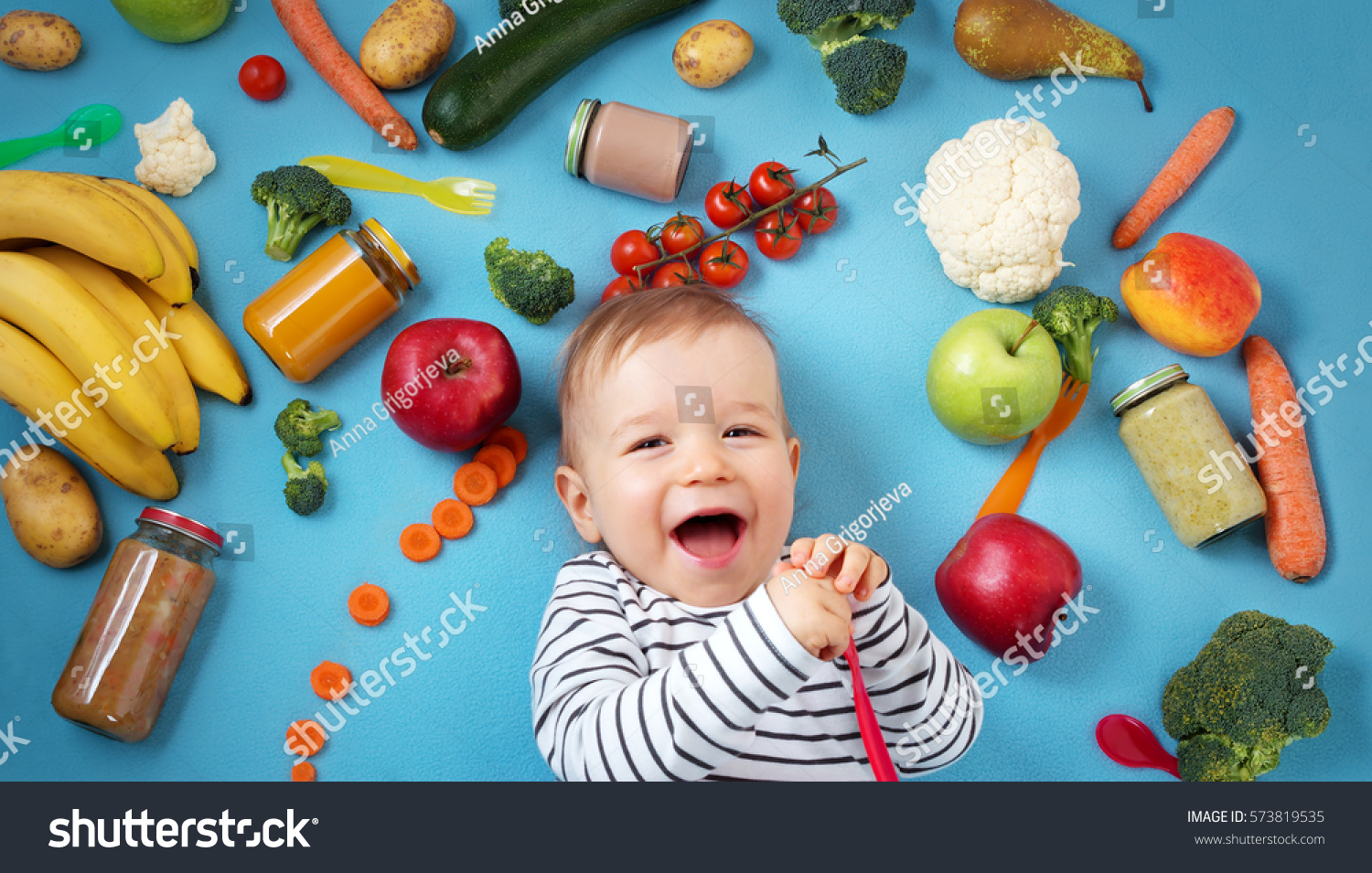baby surrounded with fruits and vegetables on blue blanket, healthy child nutrition #573819535