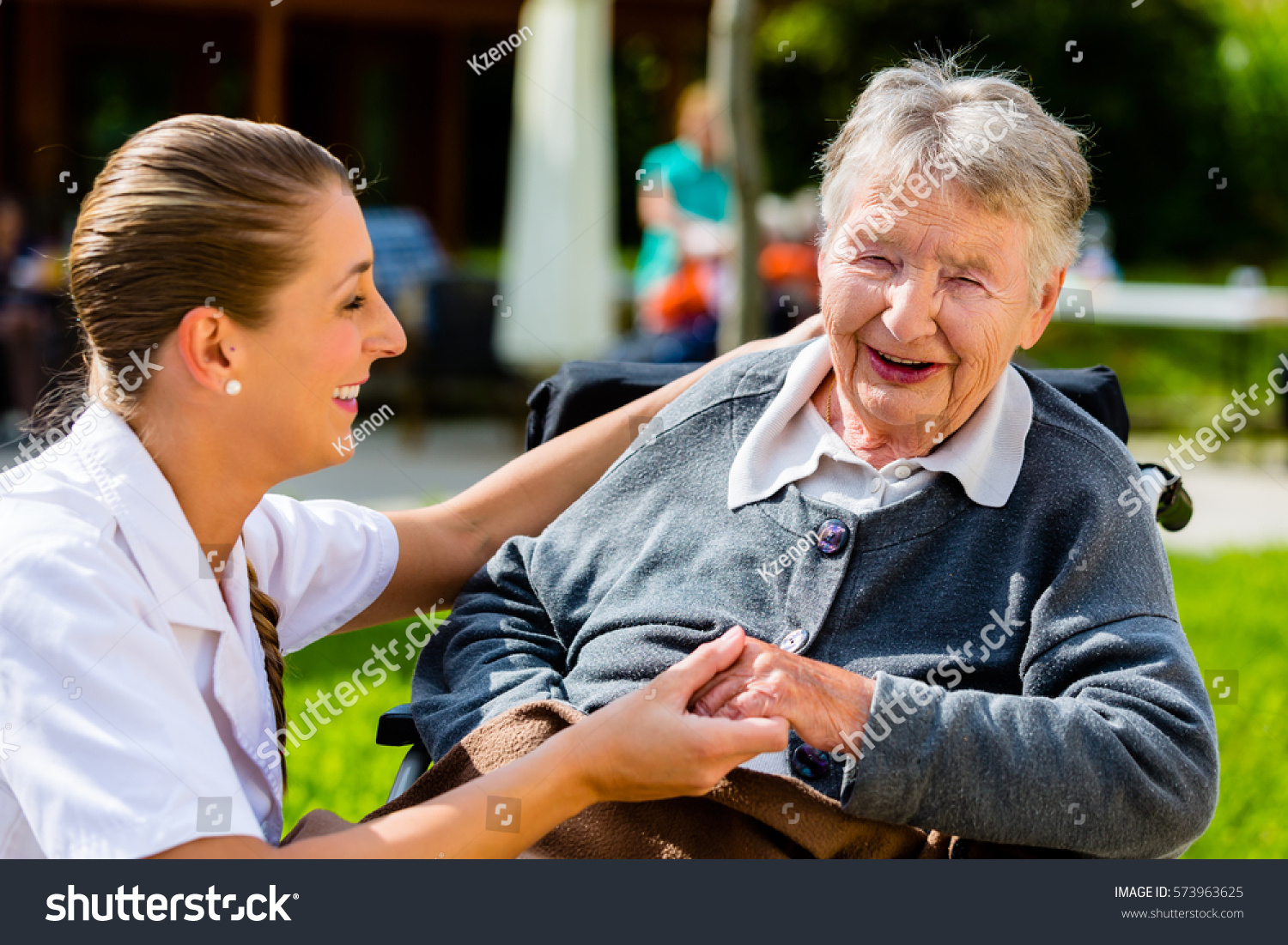 Nurse holding hands with senior woman sitting in wheelchair in garden of retirement home #573963625