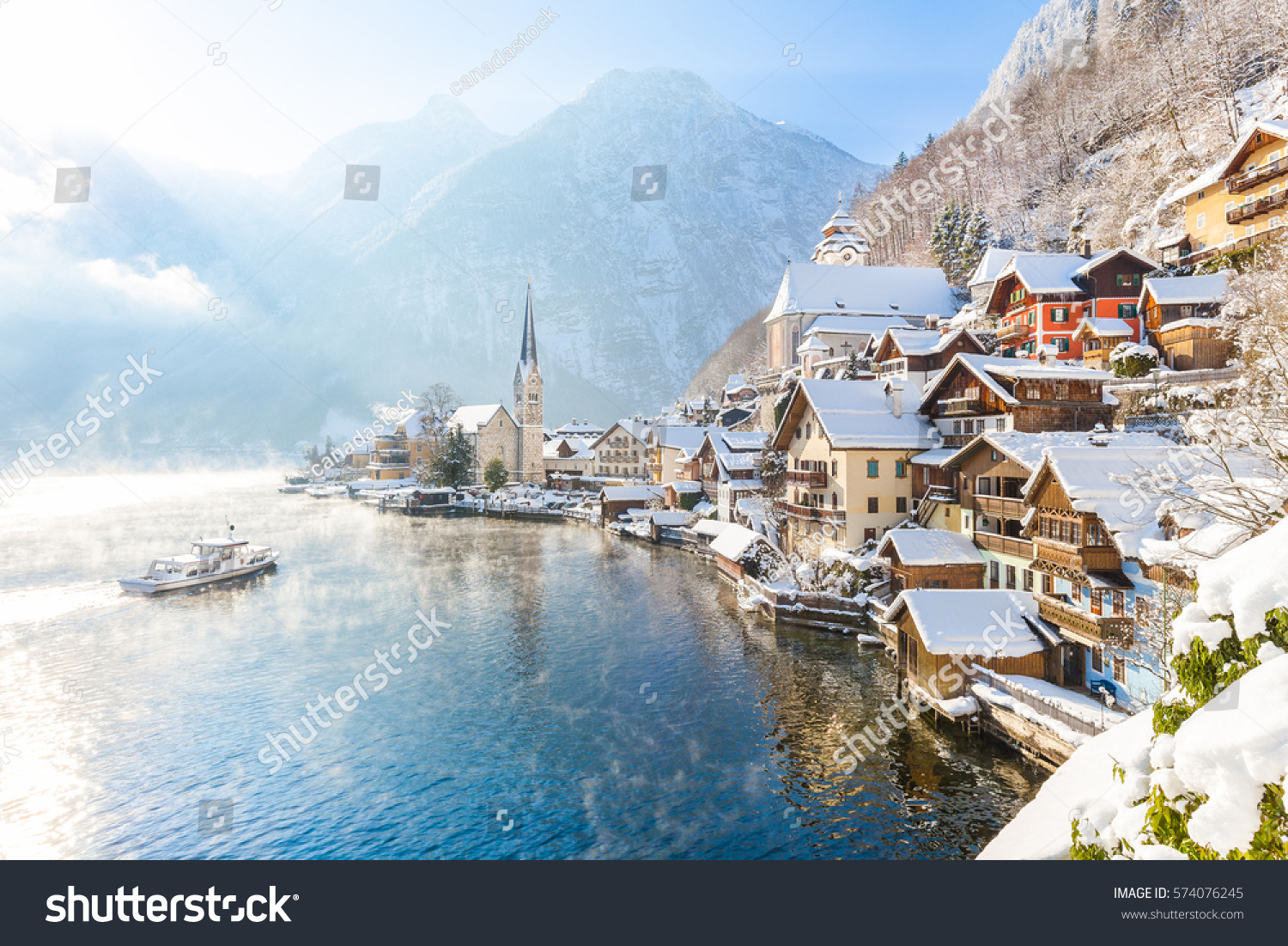 Classic postcard view of famous Hallstatt lakeside town in the Alps with traditional passenger ship on a beautiful cold sunny day with blue sky and clouds in winter, Salzkammergut region, Austria #574076245